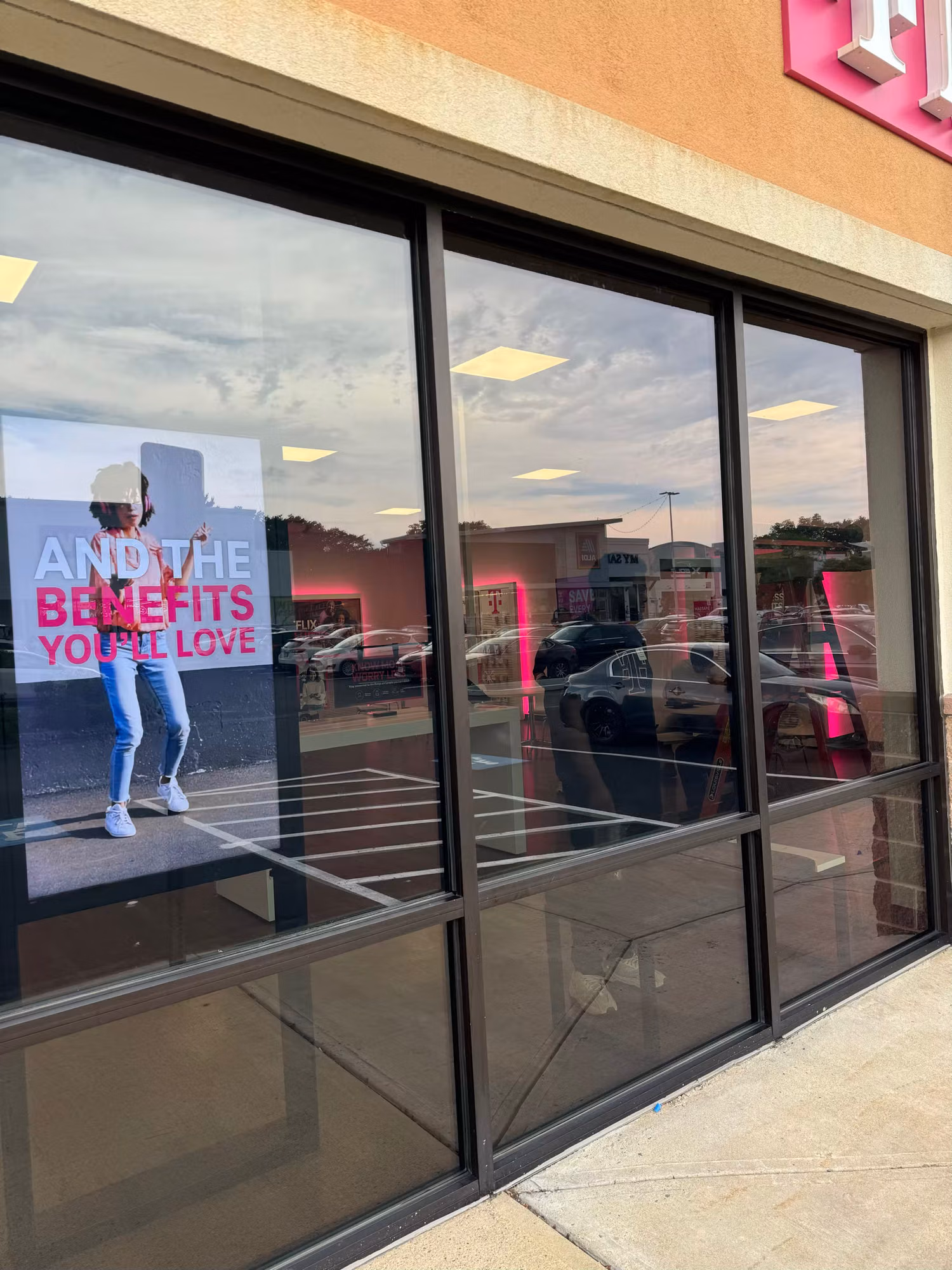 Three-panel tinted storefront display window reflecting the parking lot with interior poster visible.