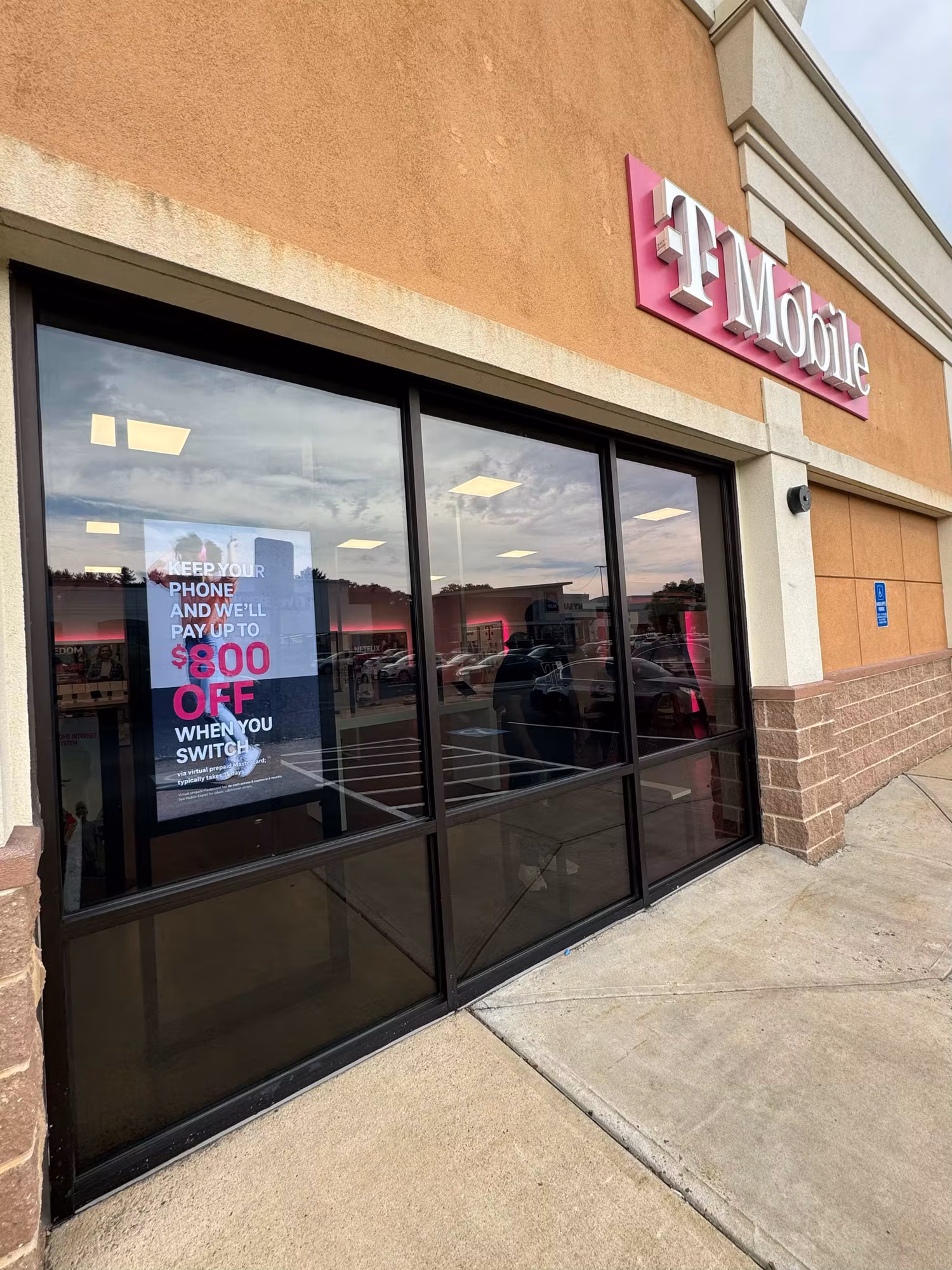 Darkly tinted multi-panel retail storefront windows beneath a lit sign reflecting the parking lot.