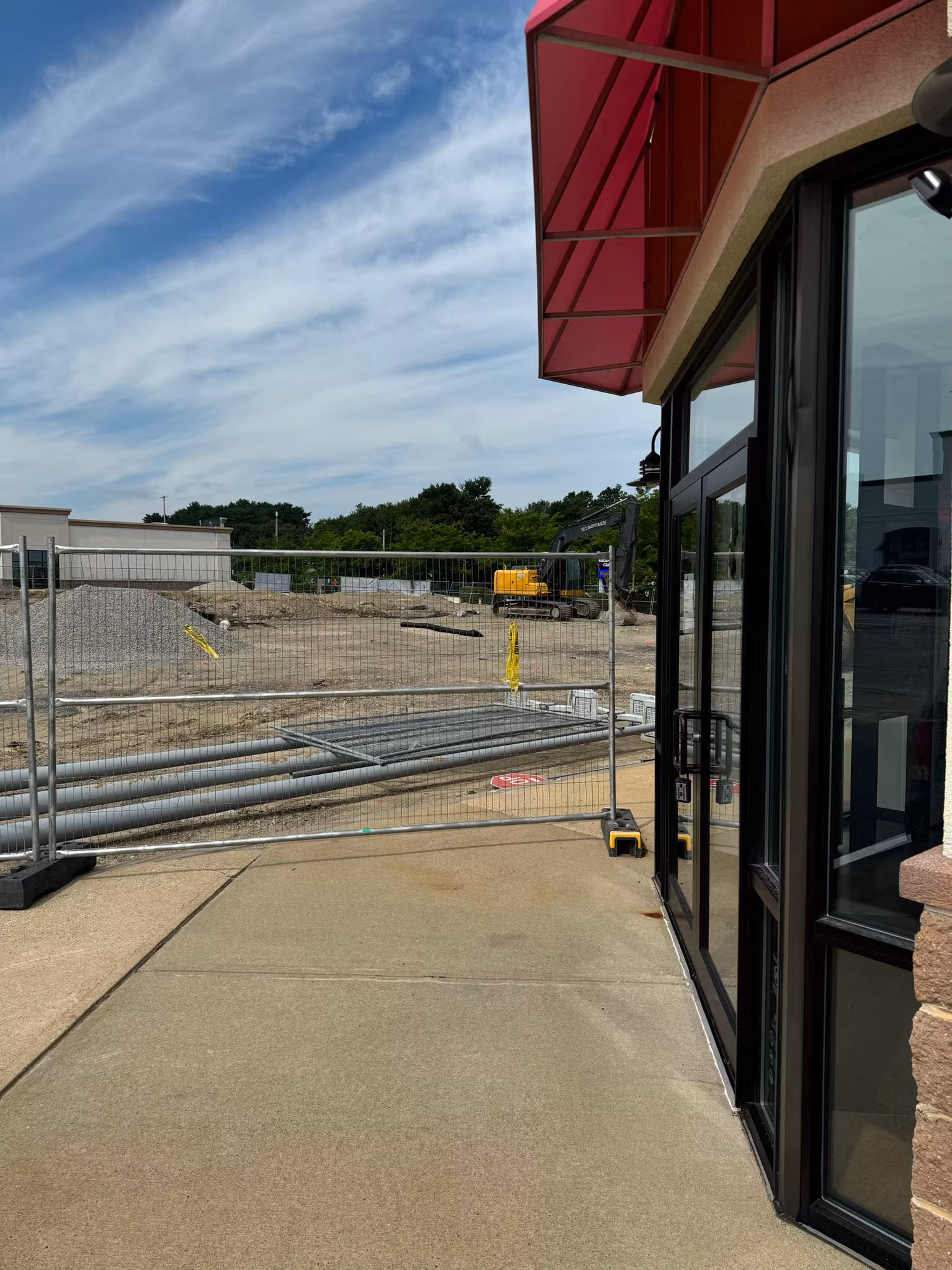 Tinted aluminum-framed glass entry door at a retail storefront looking out toward a fenced construction lot.