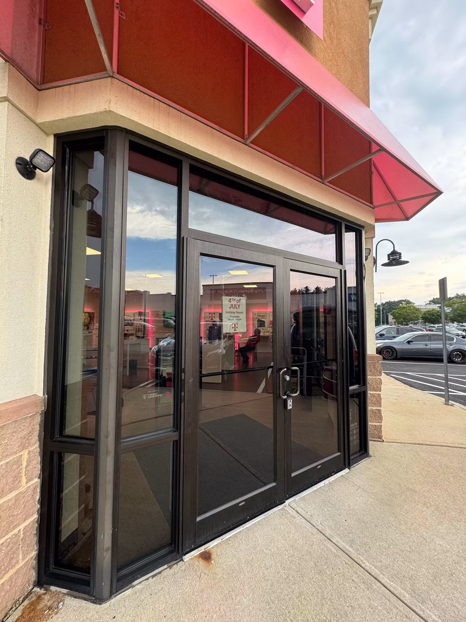 Solar-control tinted storefront entry doors and sidelight glass under a red awning at a retail shop.