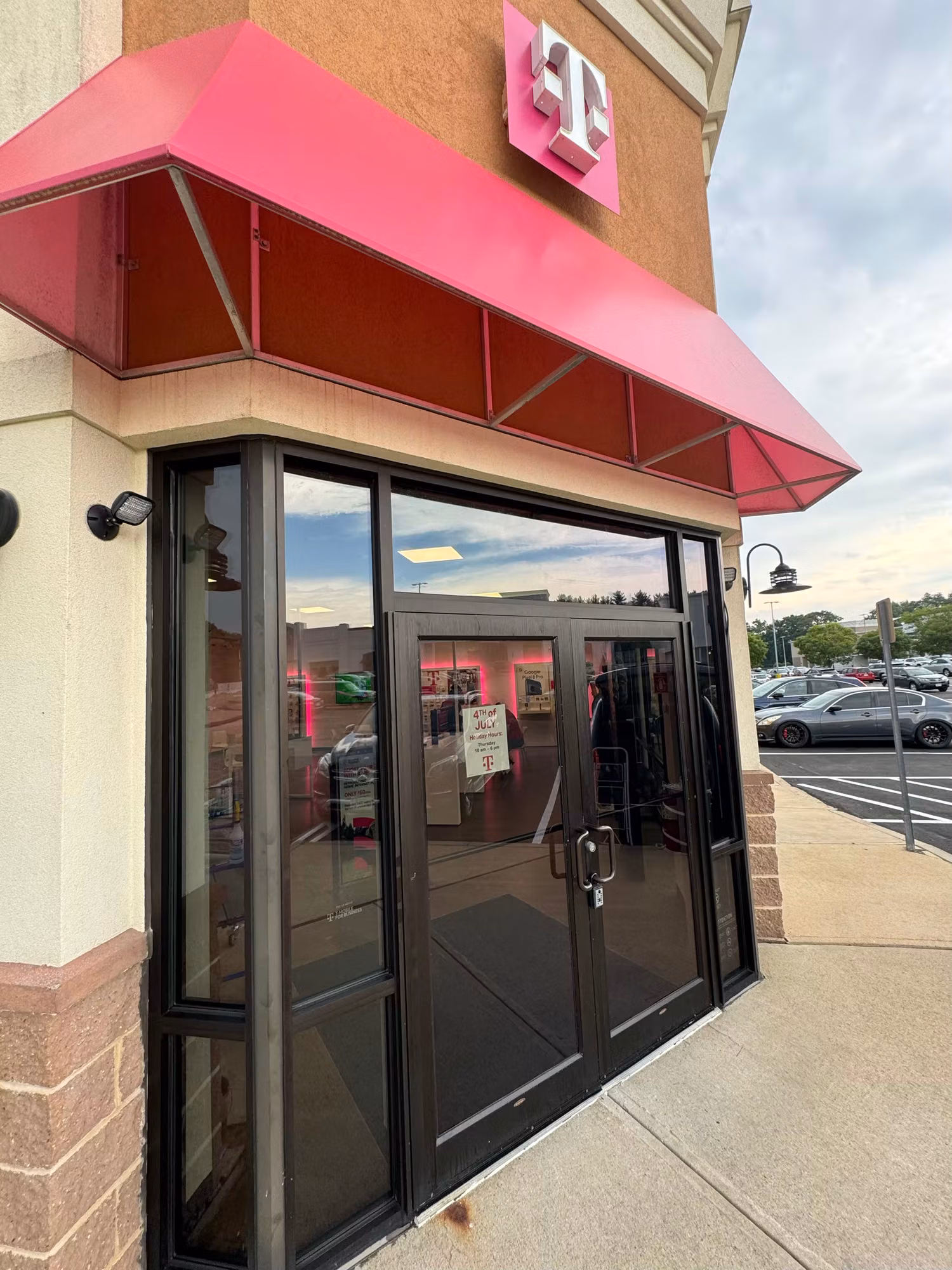 Tinted glass entry doors and sidelights at a retail storefront beneath a bright awning and lit sign.