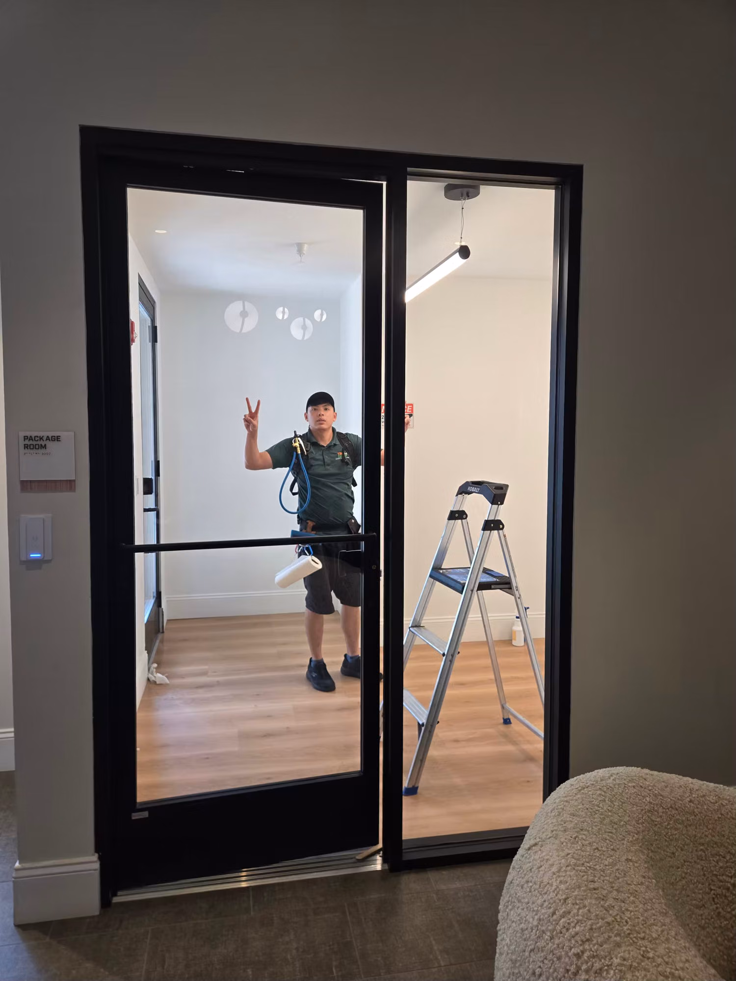Technician beside a step ladder at a black-framed glass partition door during a window film installation.