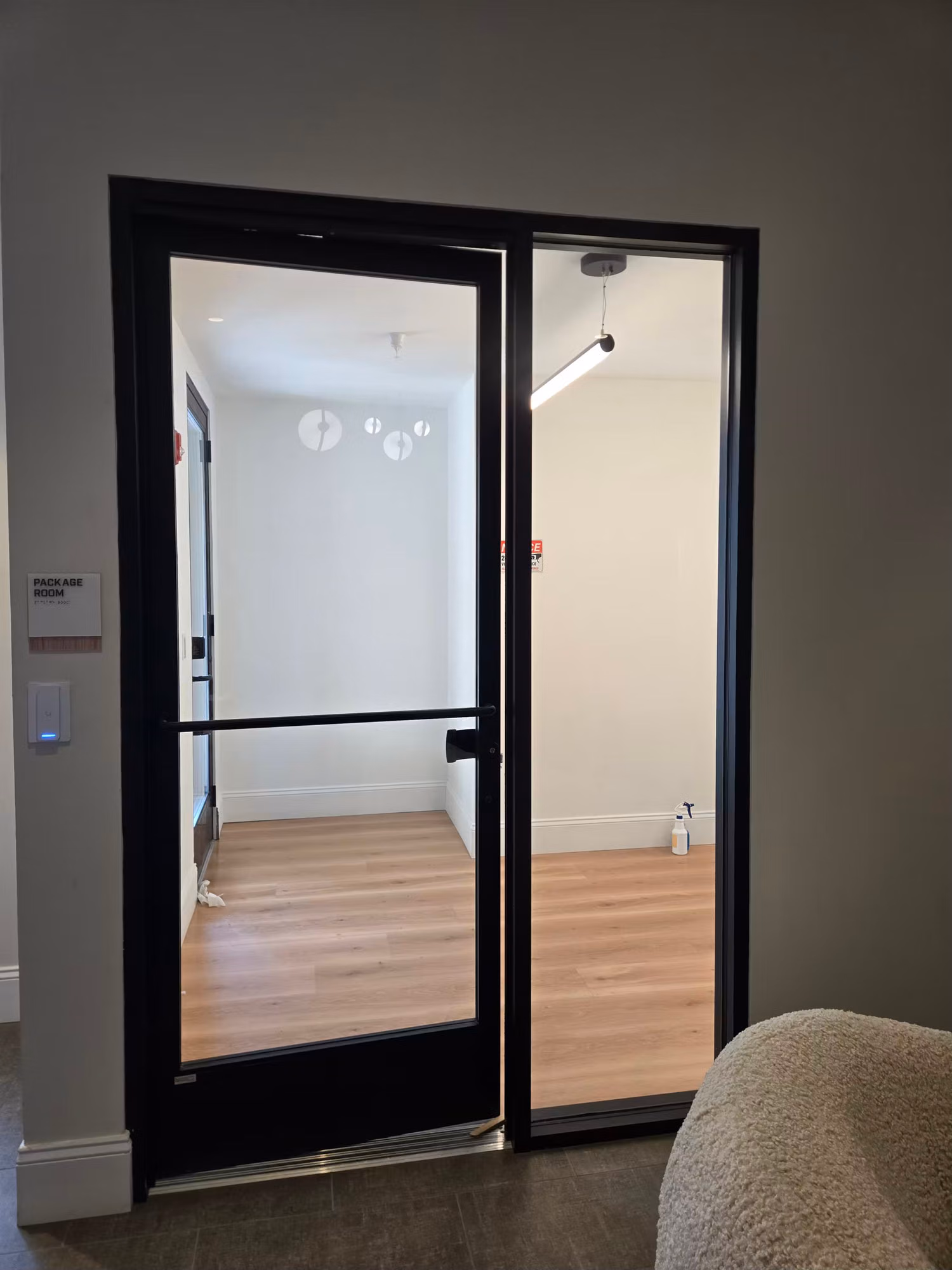 Black-framed interior glass partition door with a thin tint band on clear glass opening into a bright room.