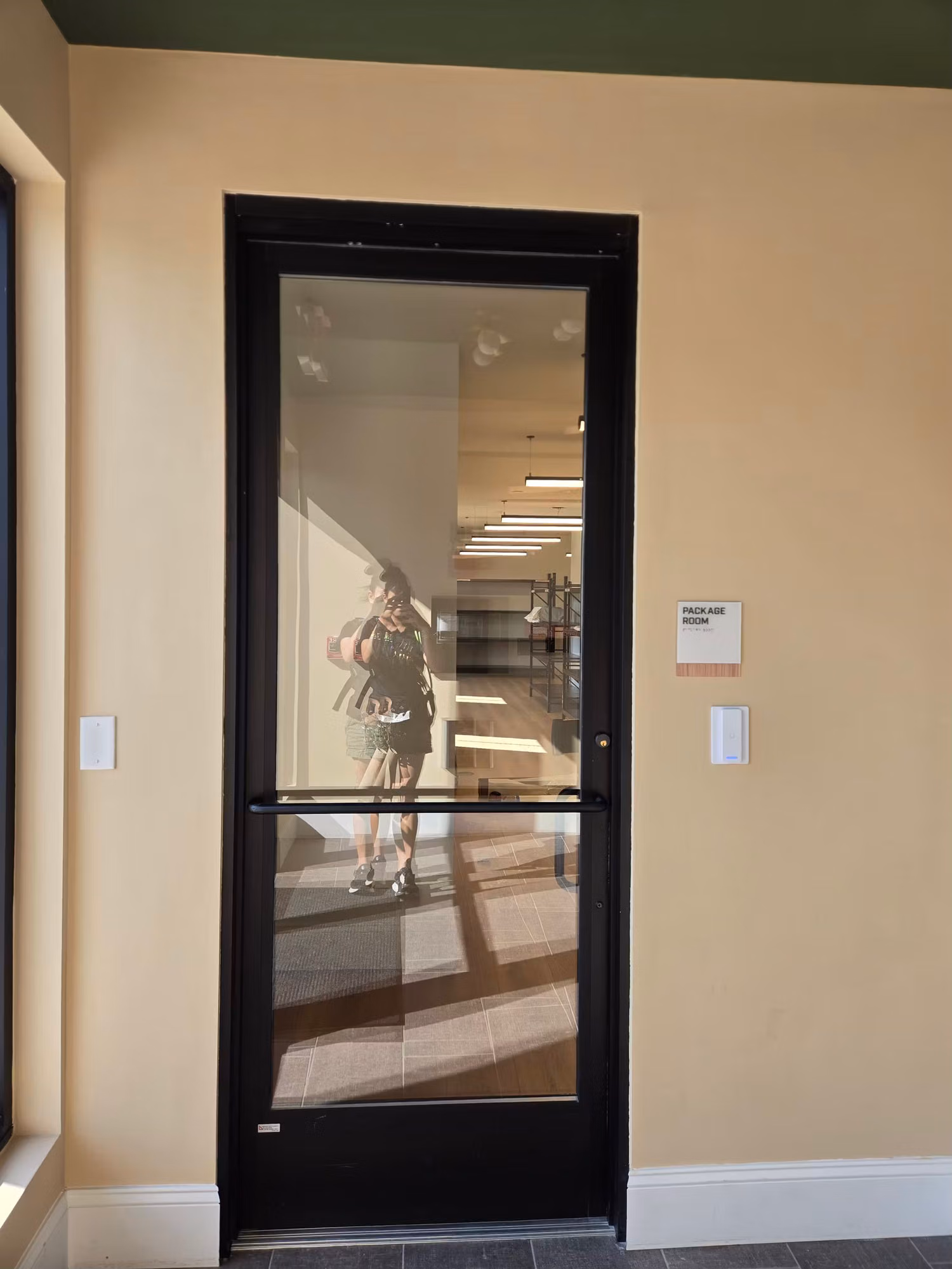 Black-framed interior glass partition door with a thin privacy tint band set into a warm-toned wall.