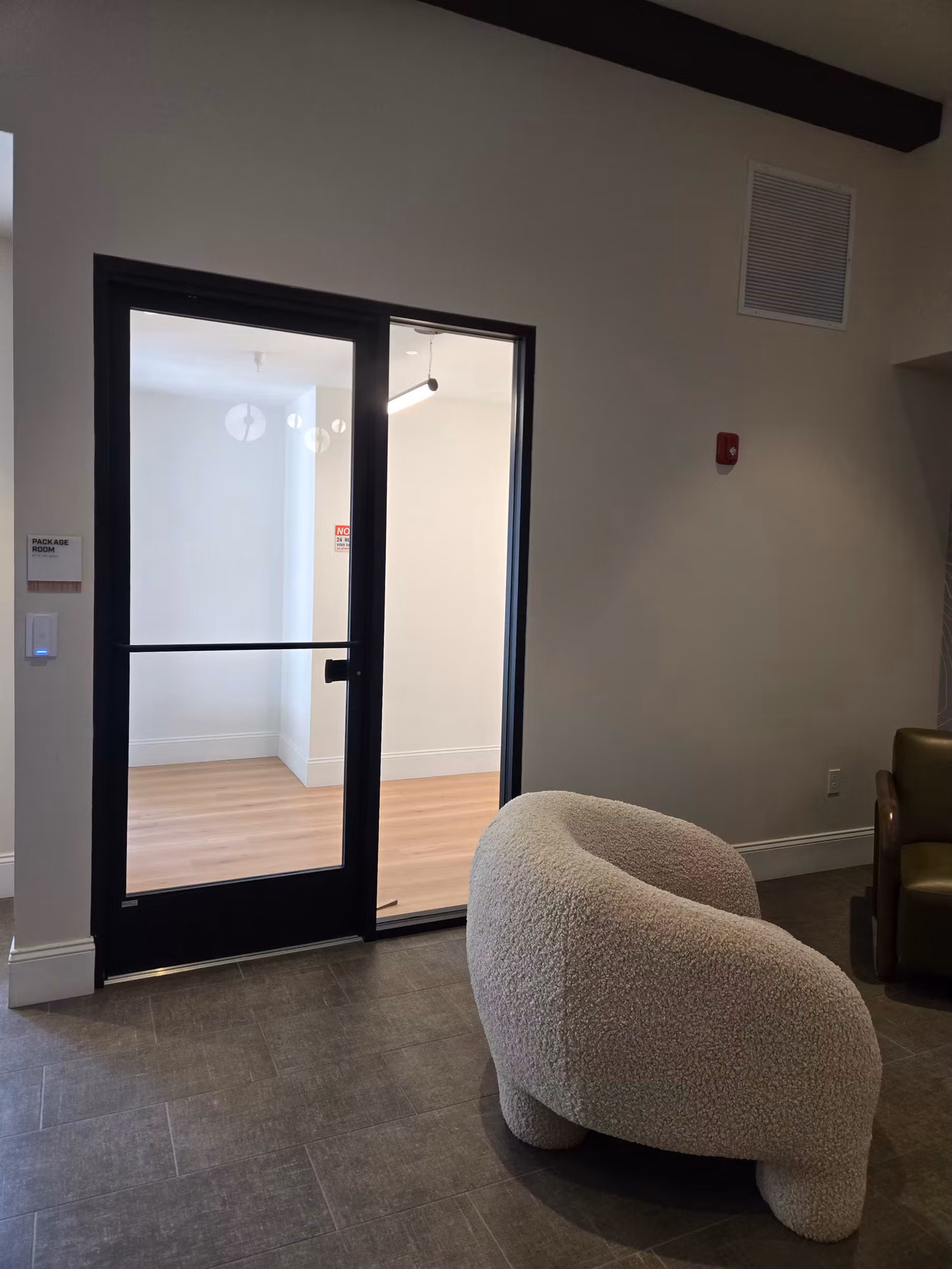 Black-framed interior glass partition door with a thin tint band opening to a hardwood-floor room.