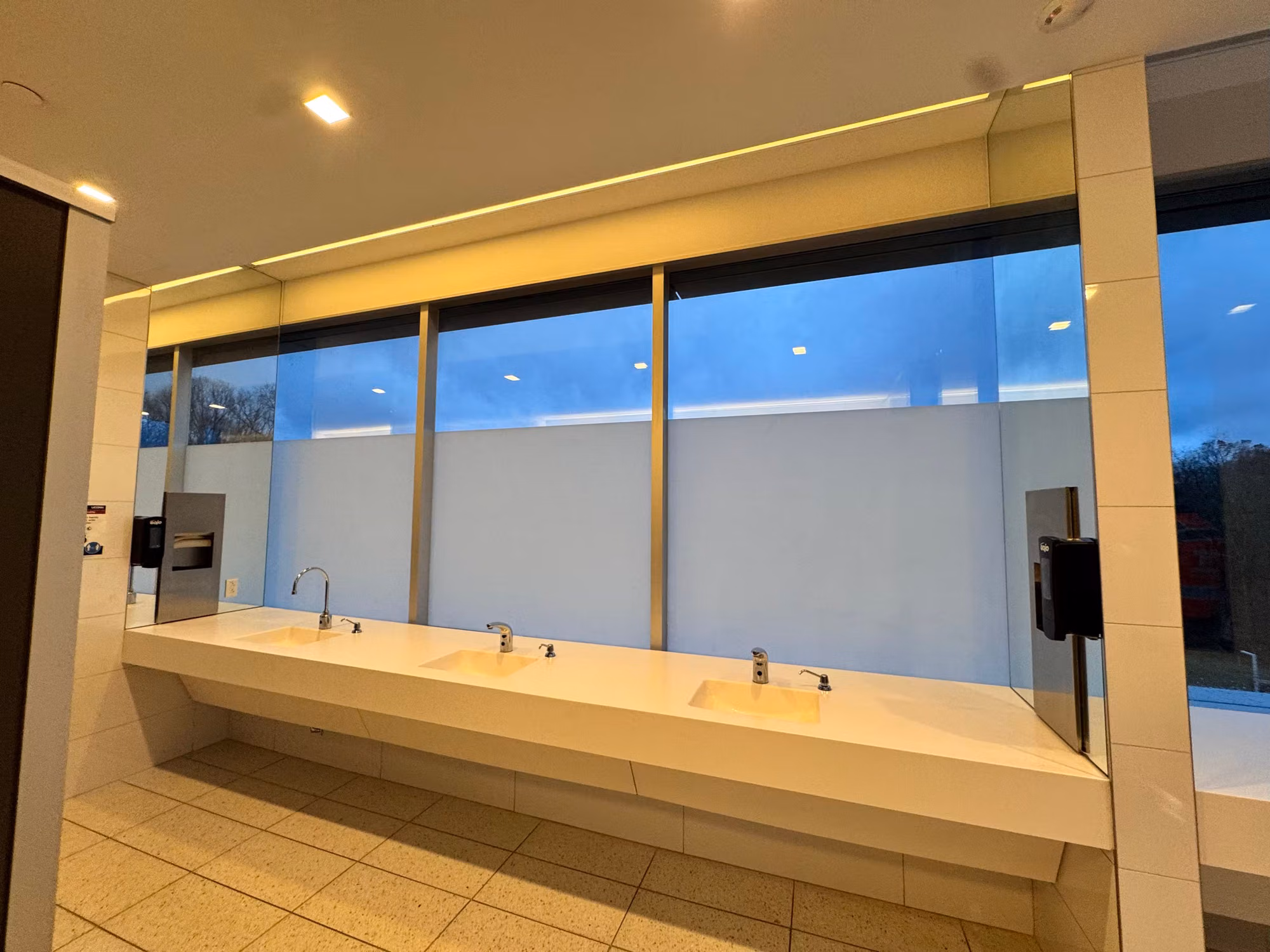 Frosted privacy band on the lower windows above a commercial restroom vanity, viewed at dusk.