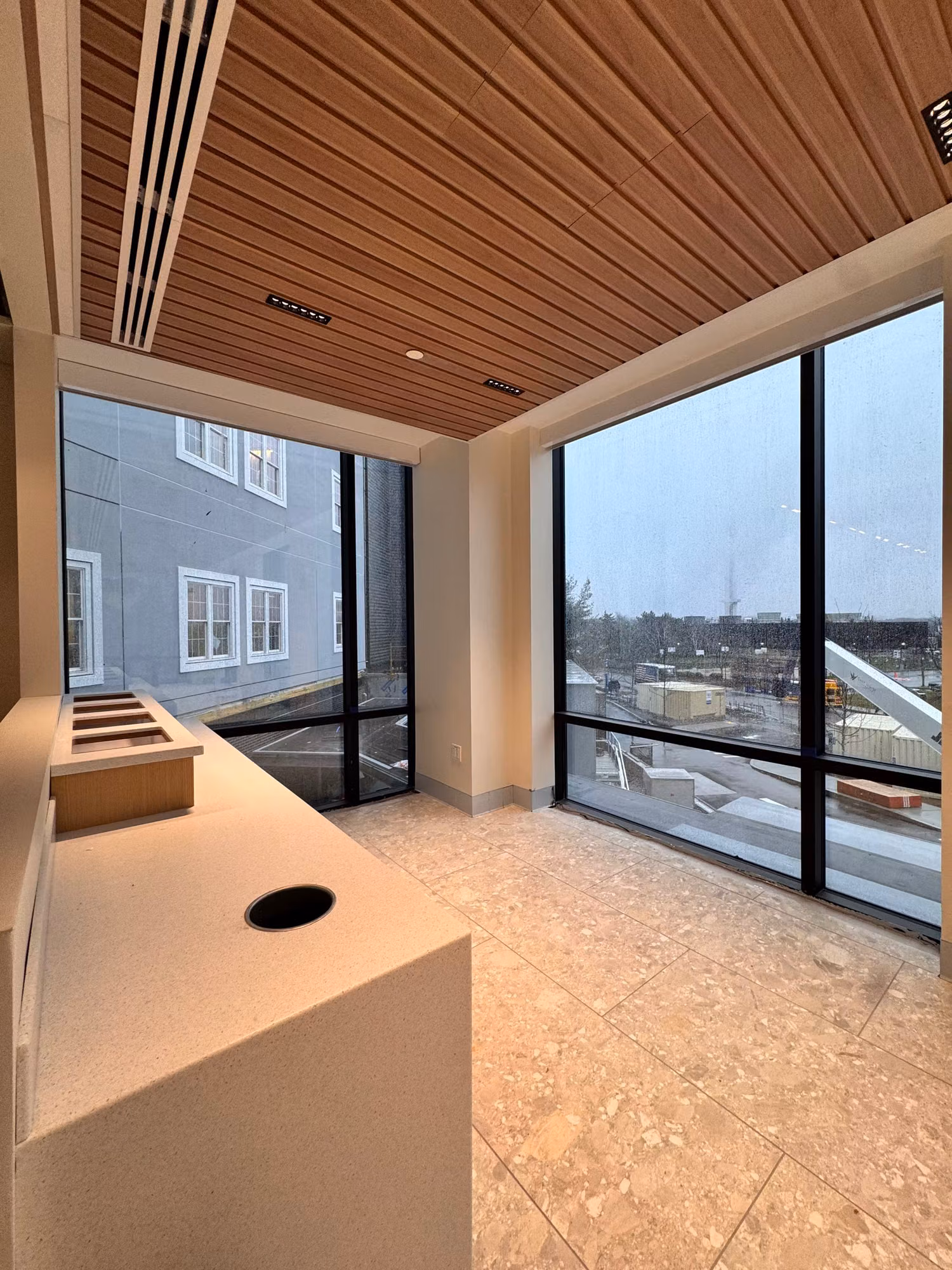 Floor-to-ceiling corner curtain-wall glazing in a modern commercial lobby with a wood-slat ceiling and stone counter.