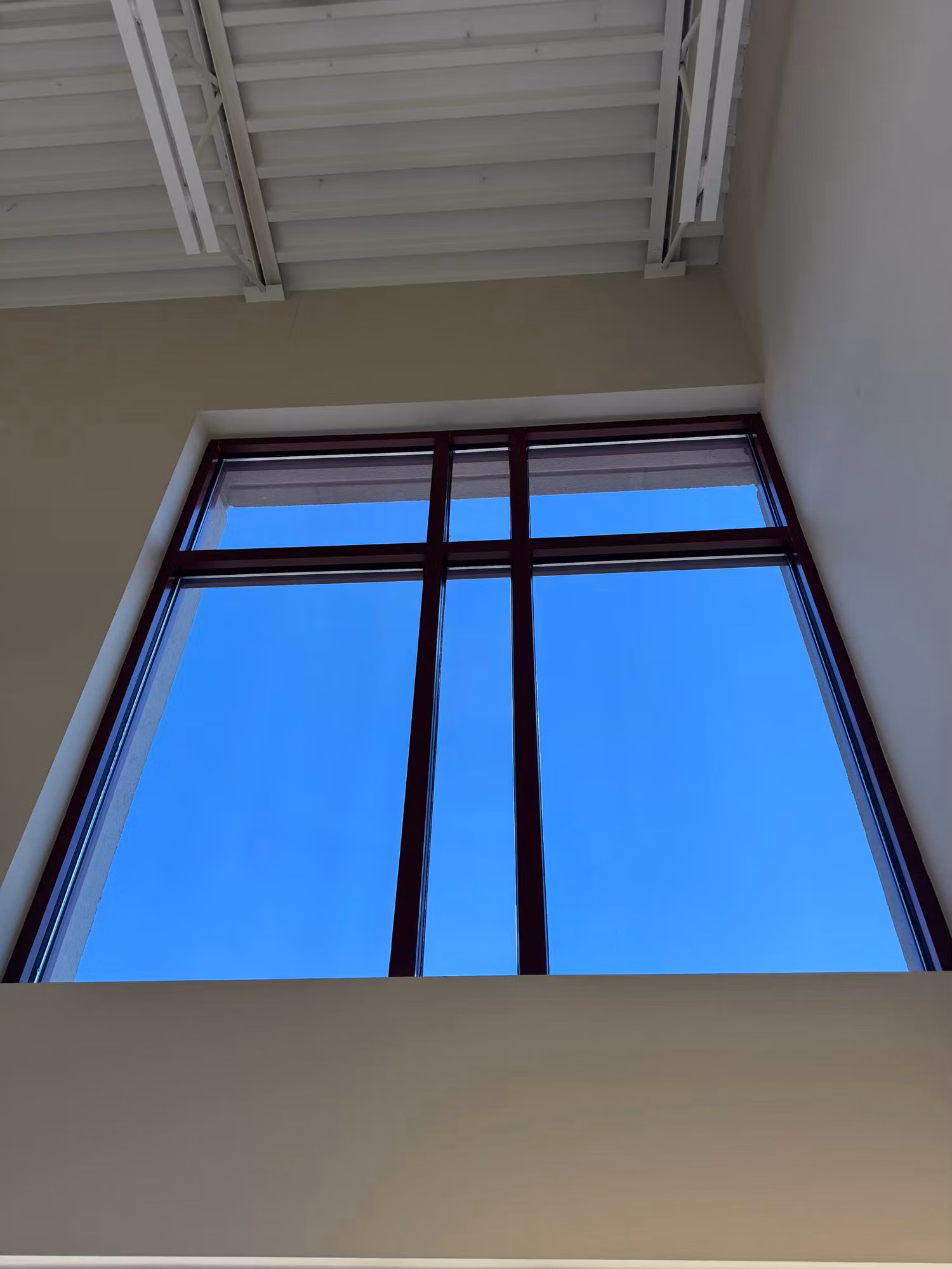 Upper clerestory commercial window with window film, framed against blue sky and exposed ceiling structure.