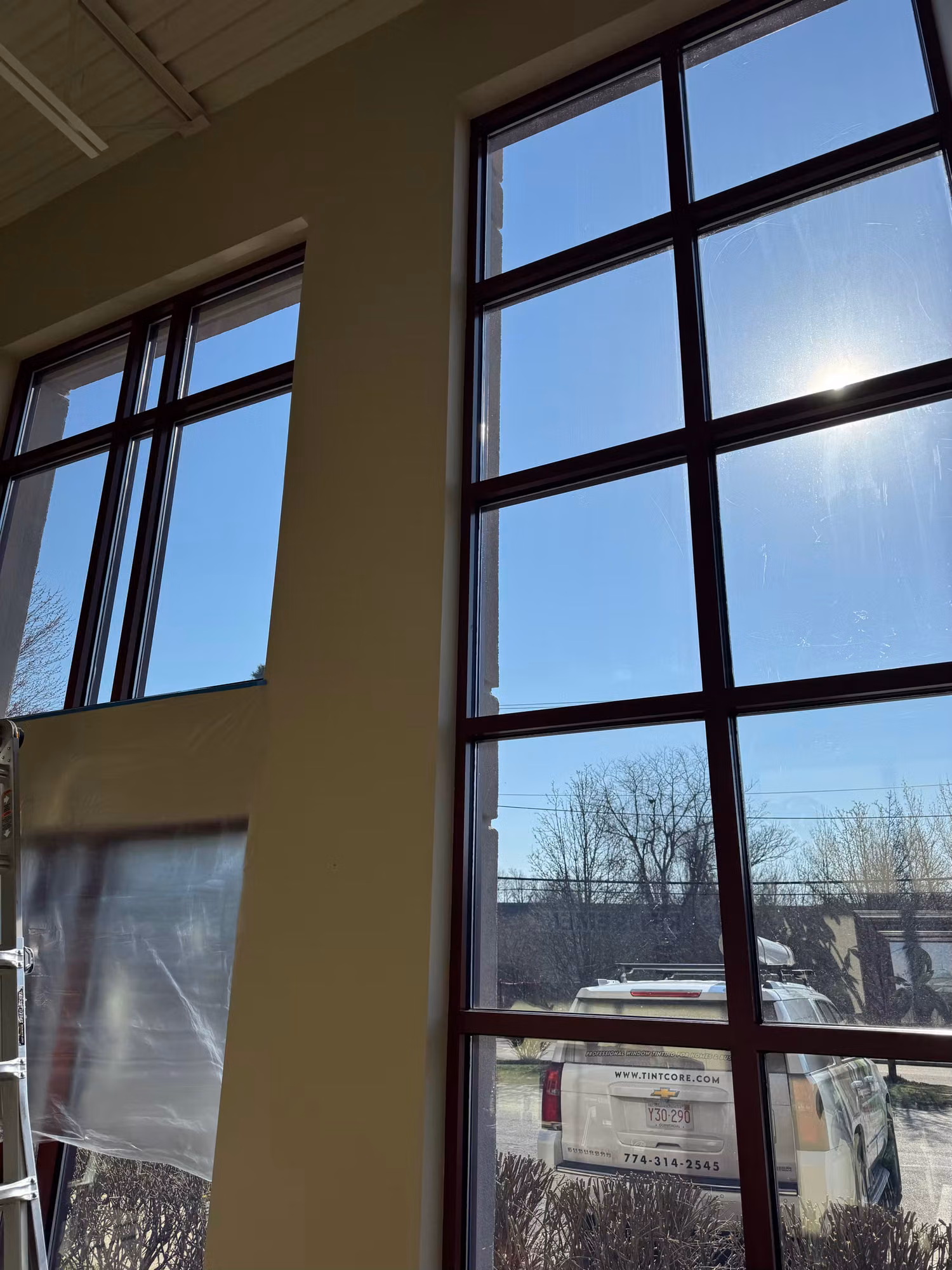Tall dark-framed two-story commercial windows with window film cutting glare from bright sun over a street view.