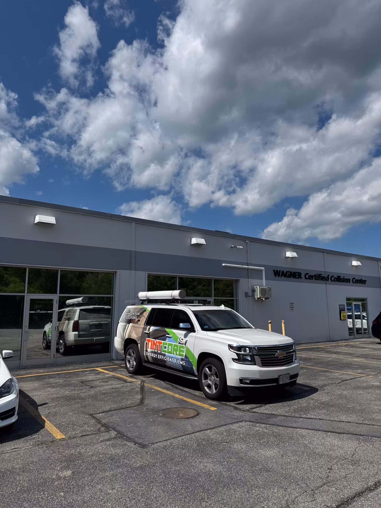 Commercial collision-center building with storefront windows treated with solar-control film and a service vehicle parked outside.