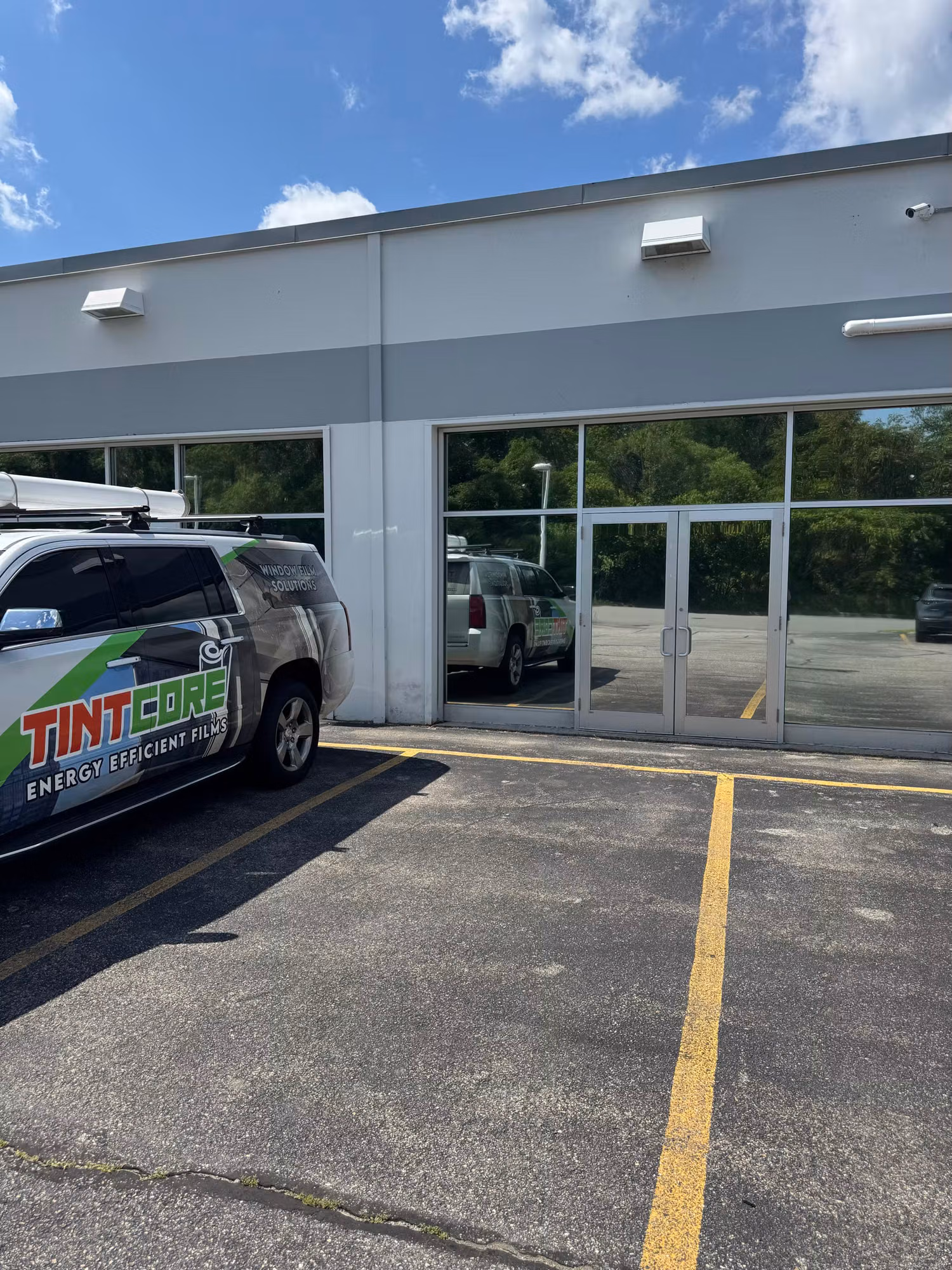 Commercial storefront windows and entry doors with darkened solar-control film, viewed from the parking lot beside a service vehicle.