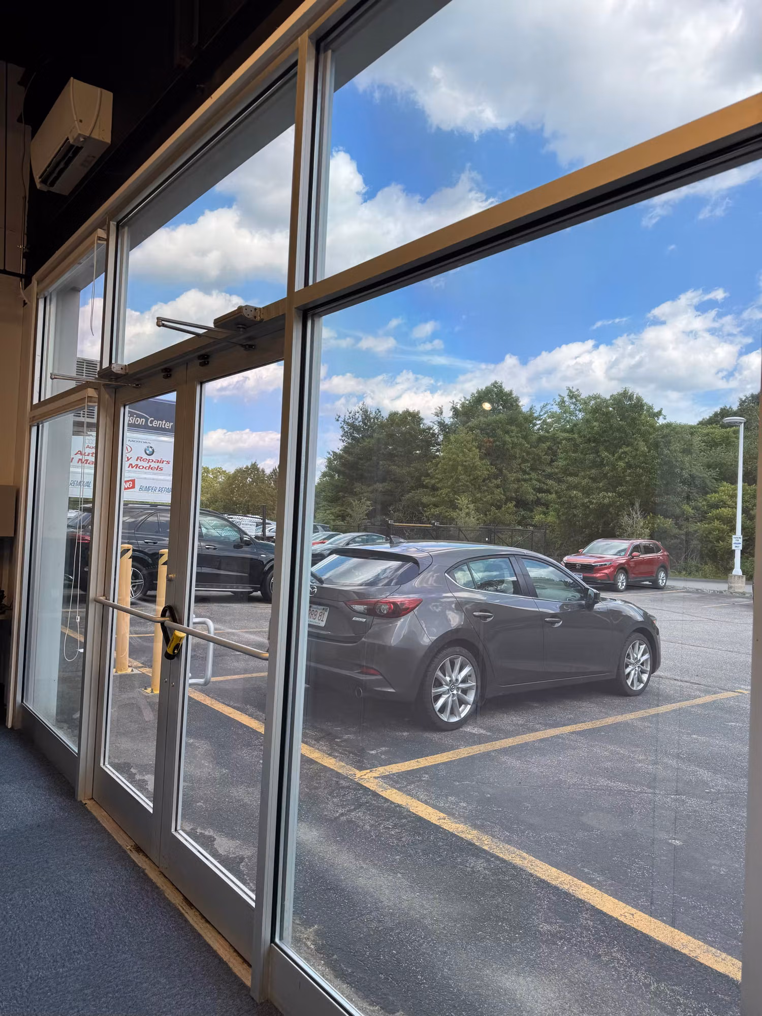 Interior view of a glass entry door and storefront window wall with solar film, looking out toward parked cars.