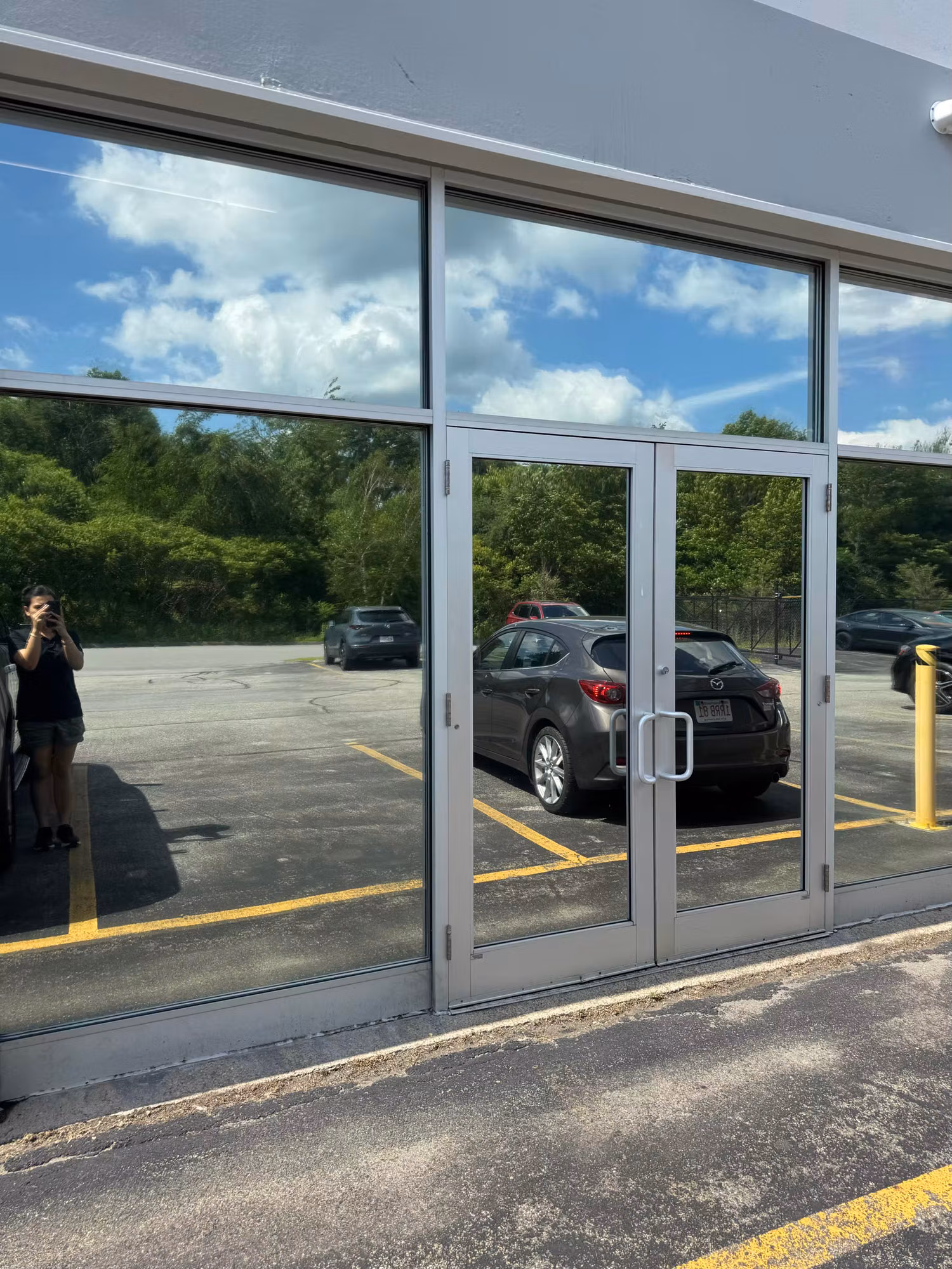 Exterior glass double doors and storefront window wall with reflective solar film mirroring the parking lot.