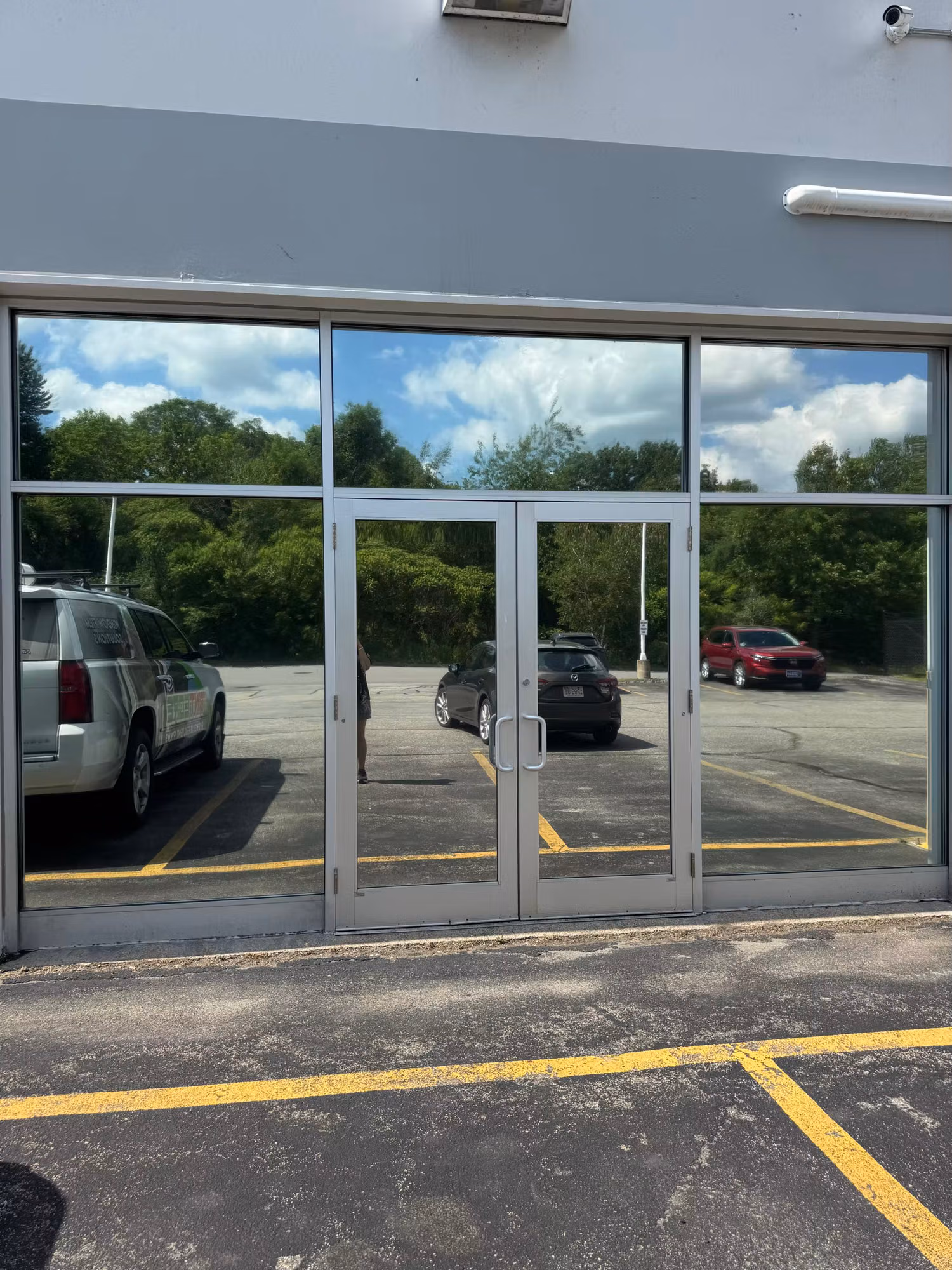 Aluminum-framed commercial storefront entry doors and sidelights with darkened reflective solar-control film mirroring the parking lot.