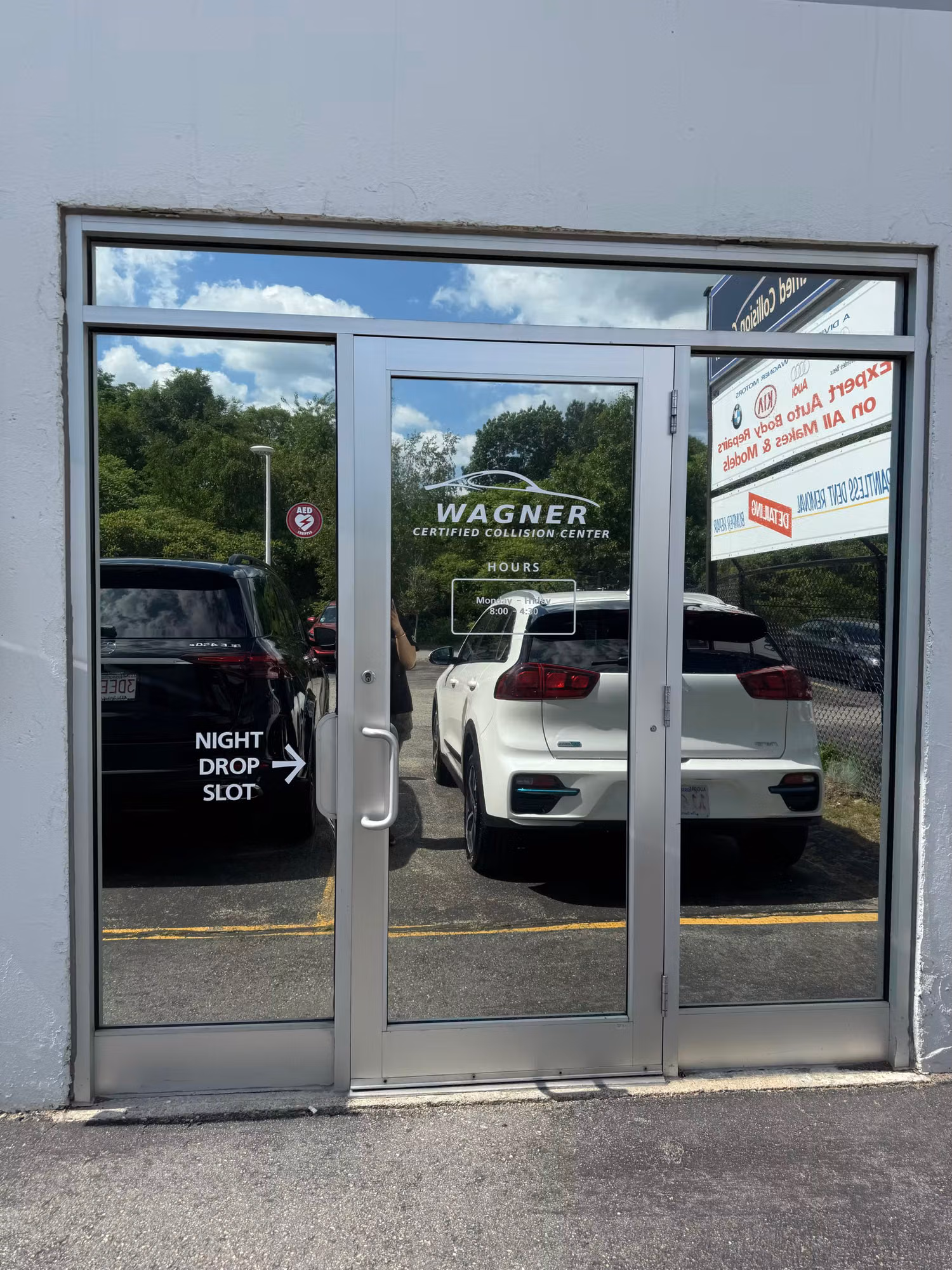 Collision-center storefront entry doors fitted with dark reflective solar-control film over the glass for heat and glare reduction.