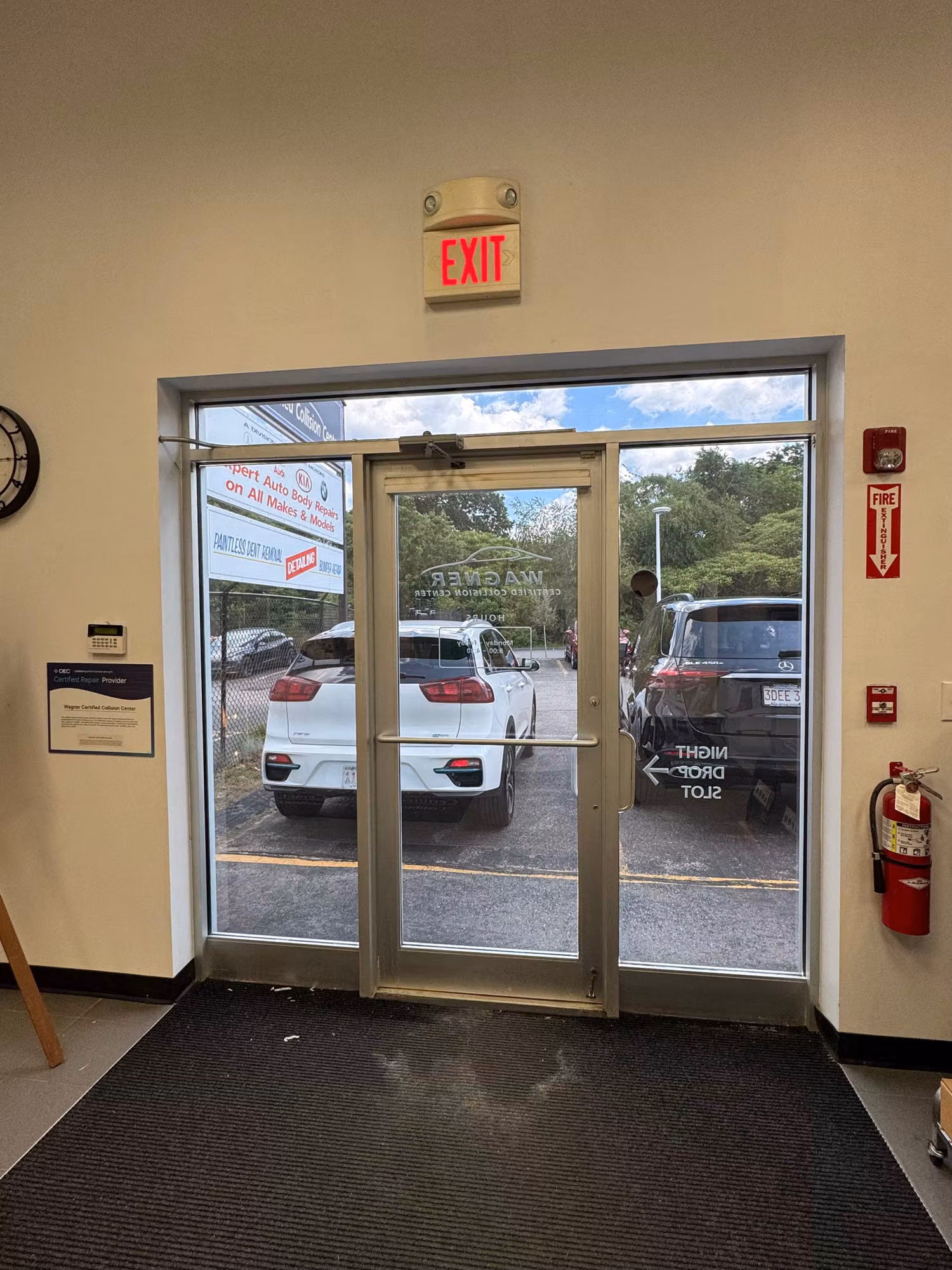 Interior view of a tinted glass exit door beneath an illuminated EXIT sign, looking out to the lot.