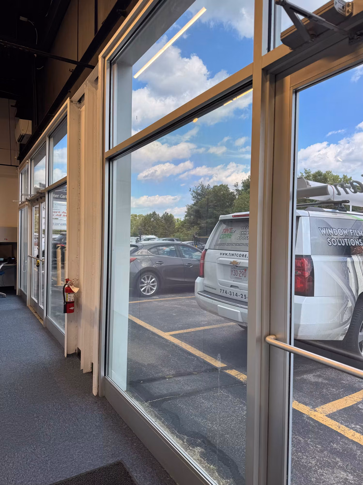 Interior view through tinted commercial storefront windows and a glass entry door overlooking the parking lot.