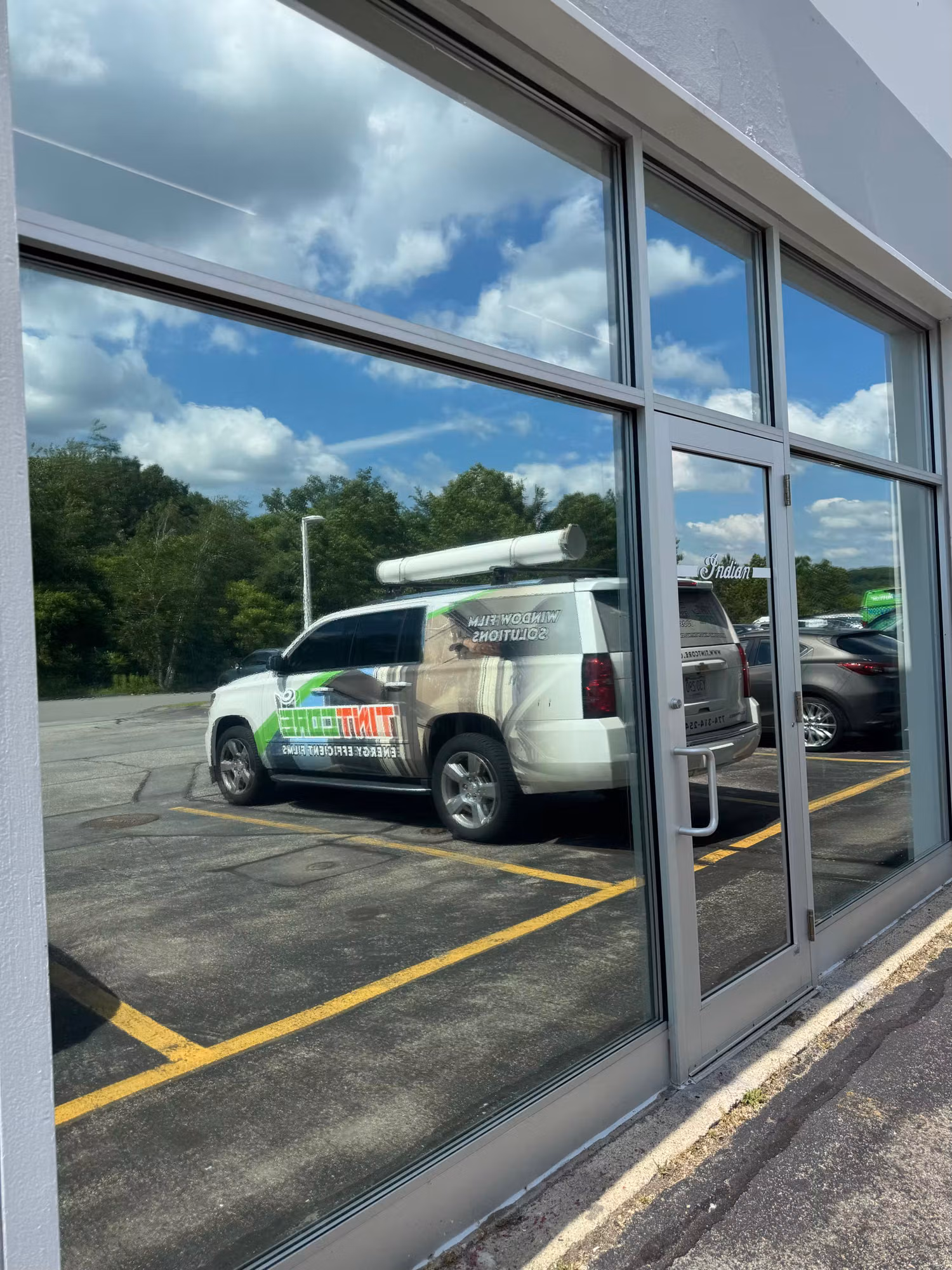 Exterior storefront window wall with reflective solar film mirroring the parking lot and sky.