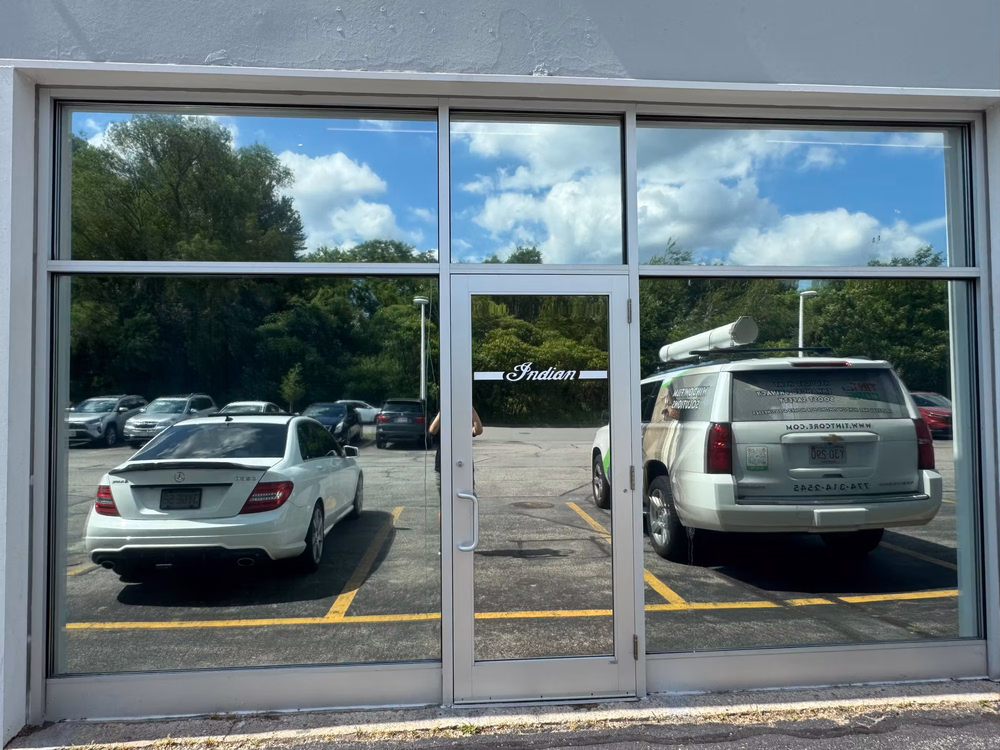 Large commercial storefront window wall and glass door with reflective solar film viewed from outside.
