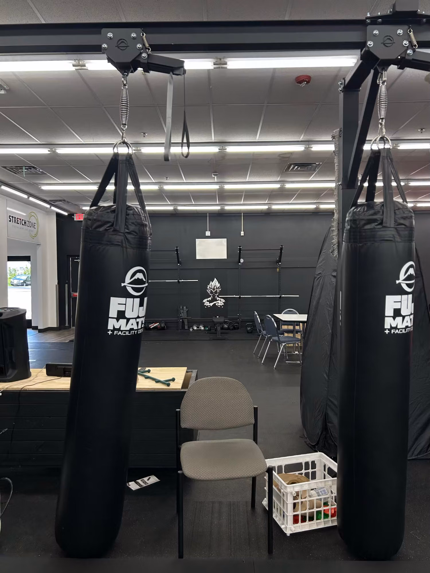 Gym interior with hanging heavy bags and a small printed graphic mounted on the far training-room wall.
