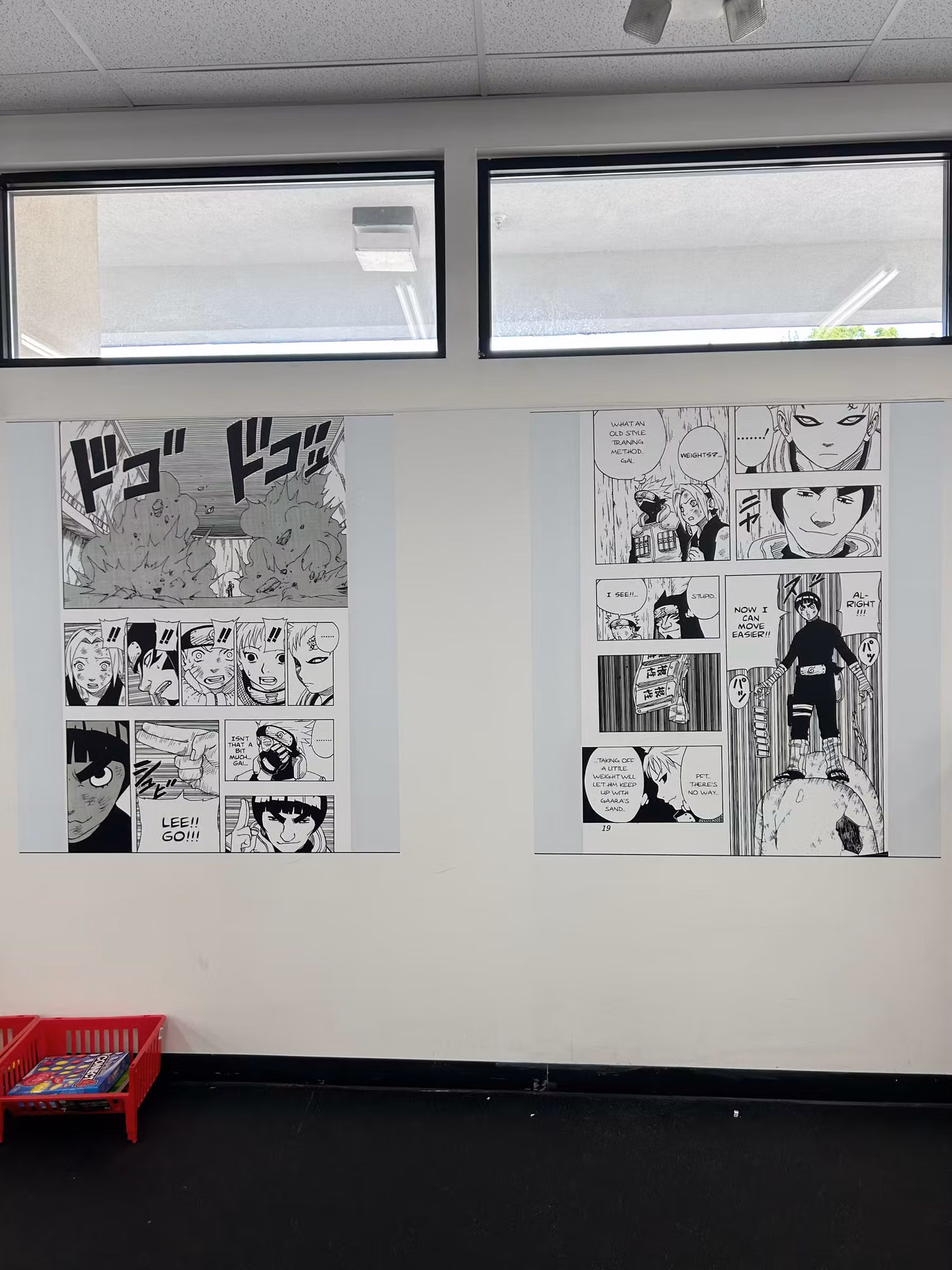 Two large manga-style printed wall wrap panels mounted on an interior gym wall beneath high windows.