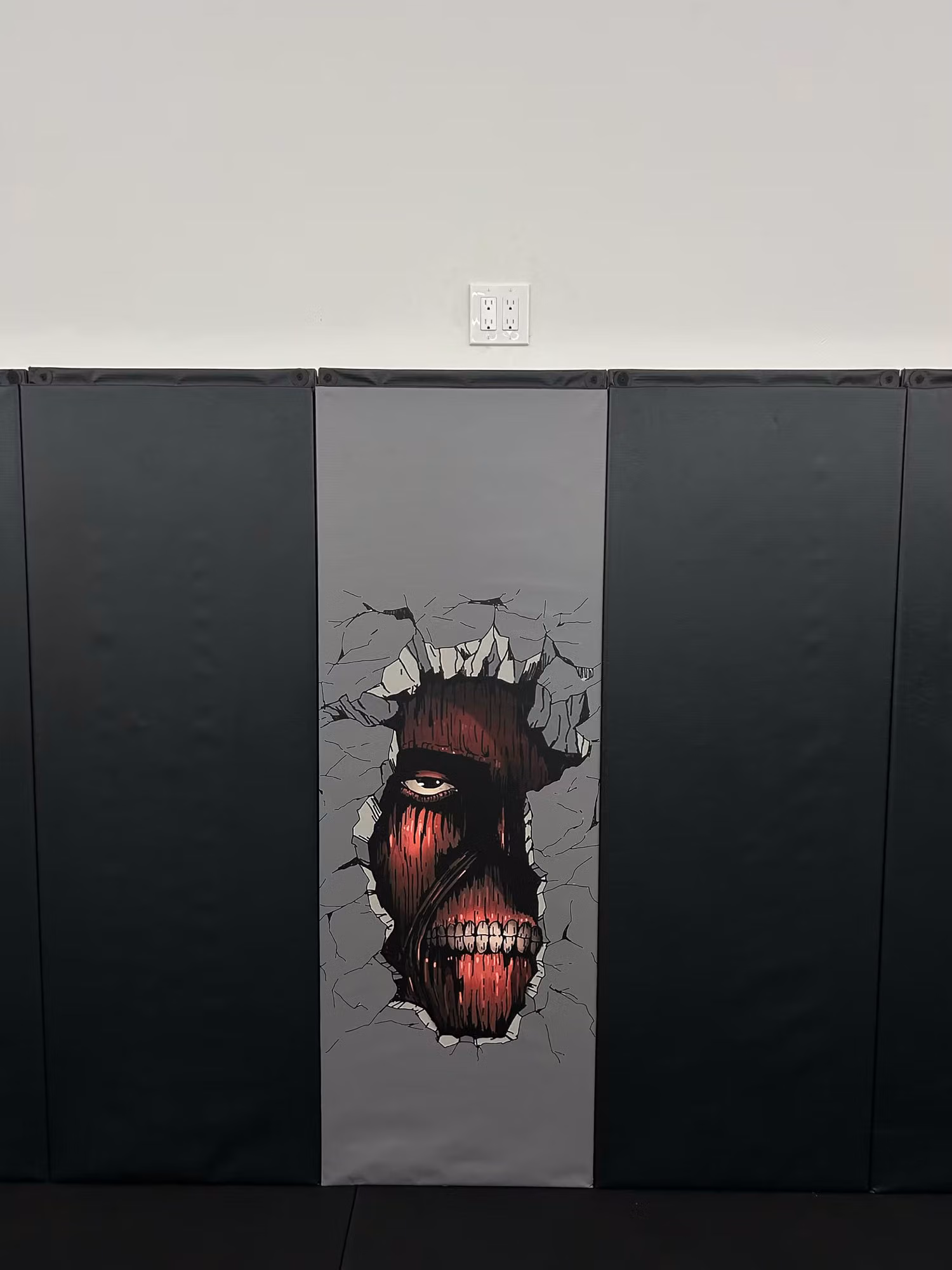 Vertical printed anime graphic panel installed on black gym wall padding between two mat sections.