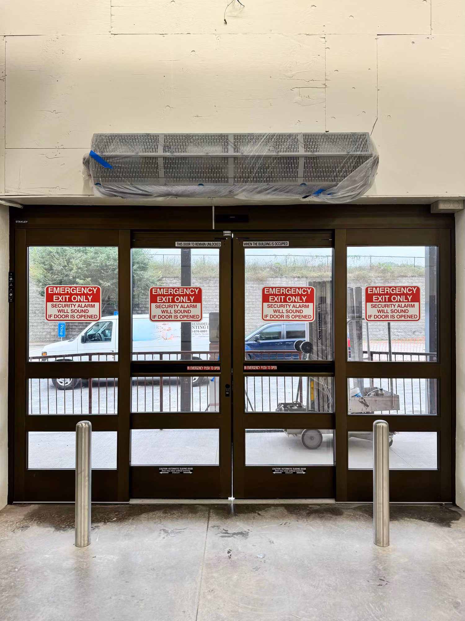 Interior view of tinted glass emergency exit doors marked Emergency Exit Only with a dark window film over the panels.