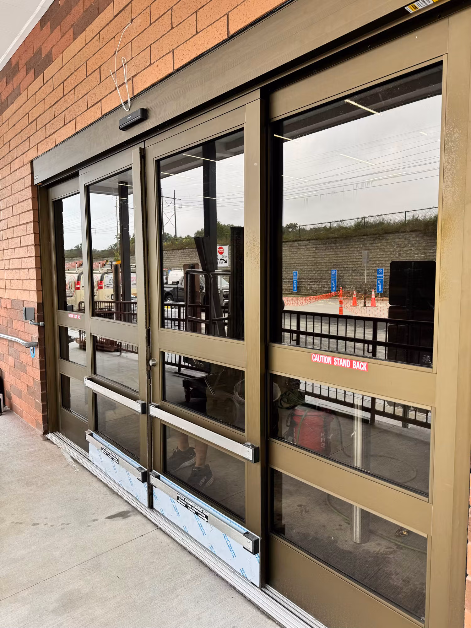 Bronze-framed automatic sliding storefront doors with darkened reflective window film along a brick exterior wall.