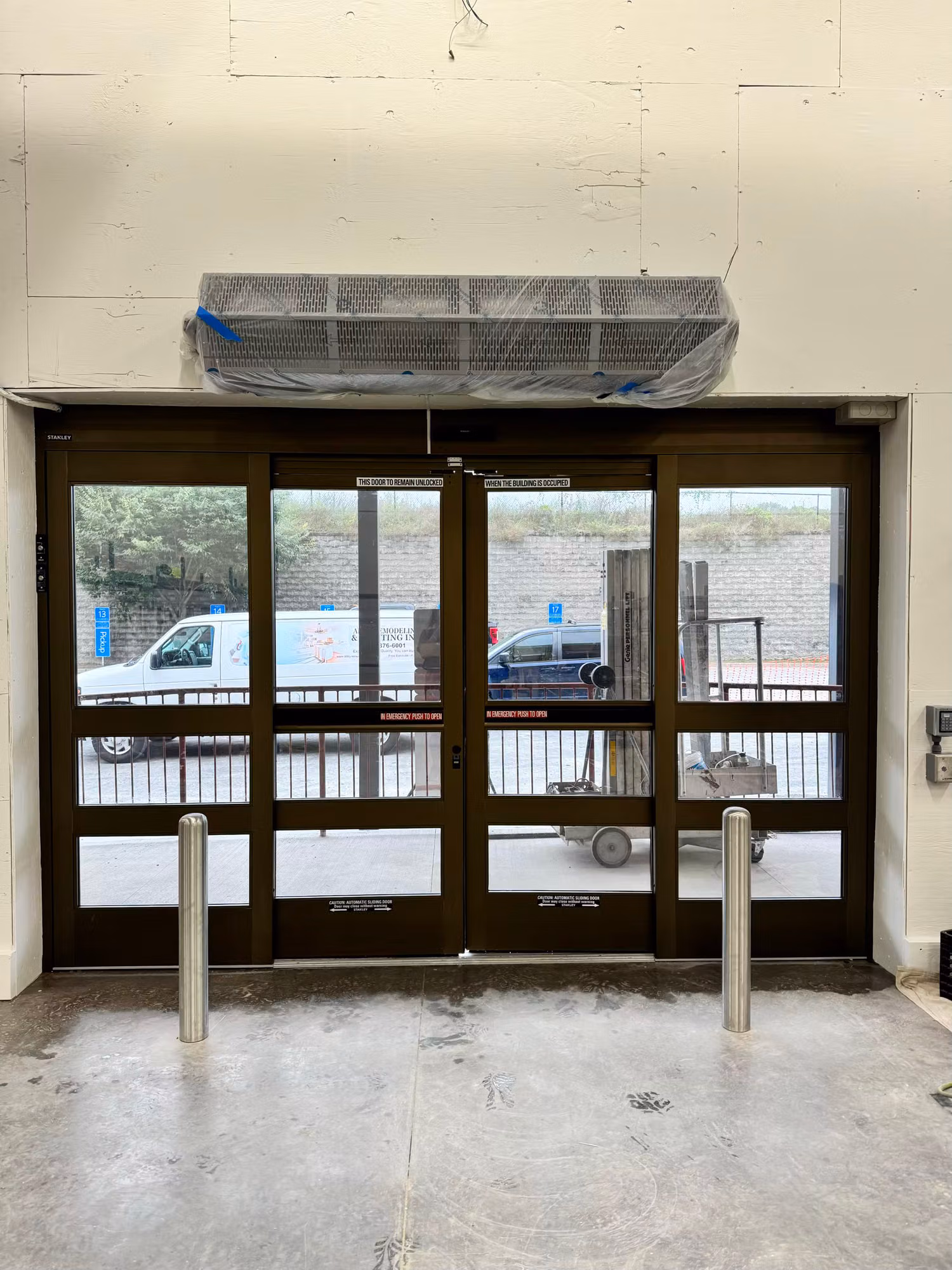 Interior view of dark-framed automatic sliding entry doors with tinted glass and bollards on a polished concrete floor.
