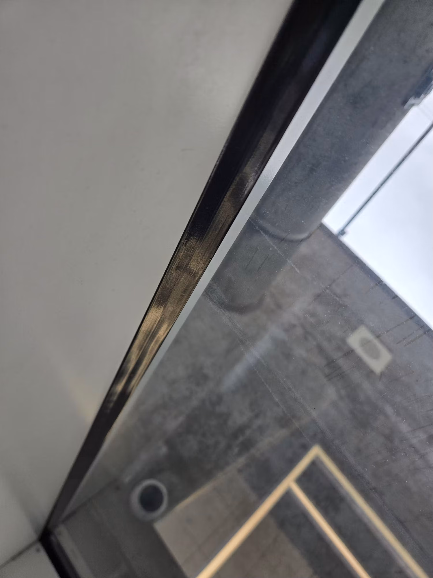 Close-up of a commercial glass window along its metal frame edge reflecting the concrete interior.