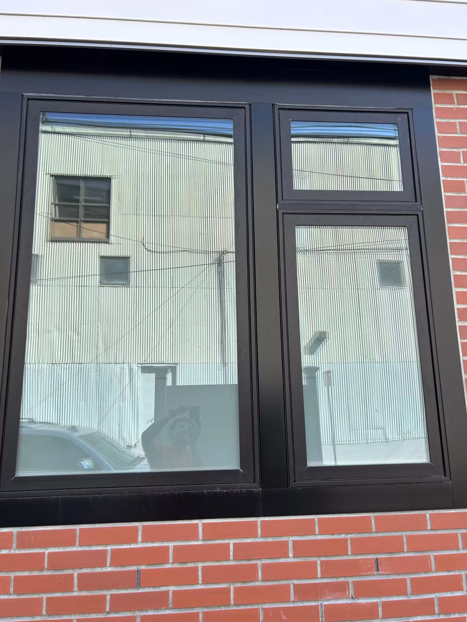 Exterior dark-framed residential window in a red brick wall with tinted glass reflecting the surroundings.