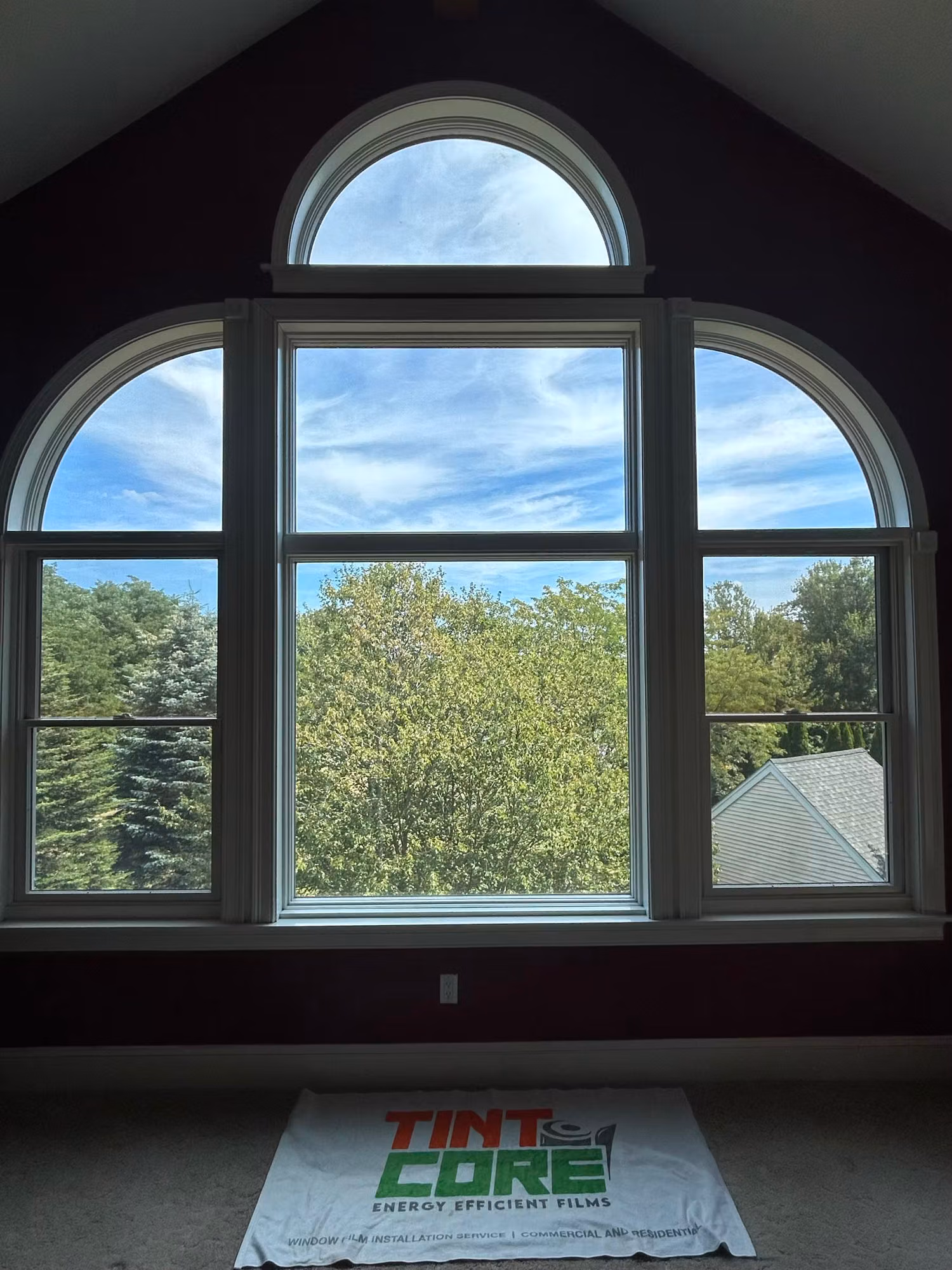 A tall arched Palladian window overlooking trees, with an installer drop cloth laid out on the floor below.