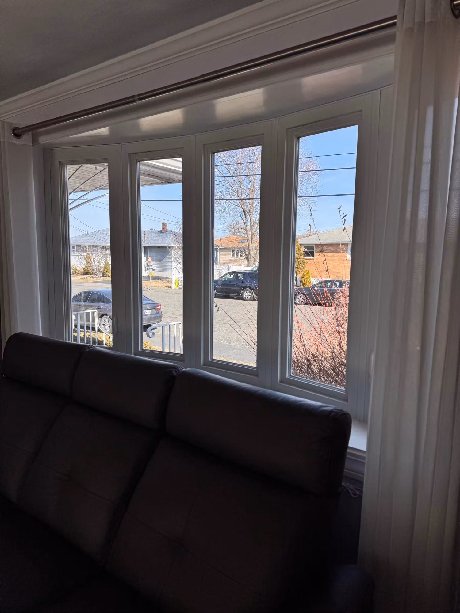 Four-pane bay window in a living room above a leather sofa looking out onto a residential street.