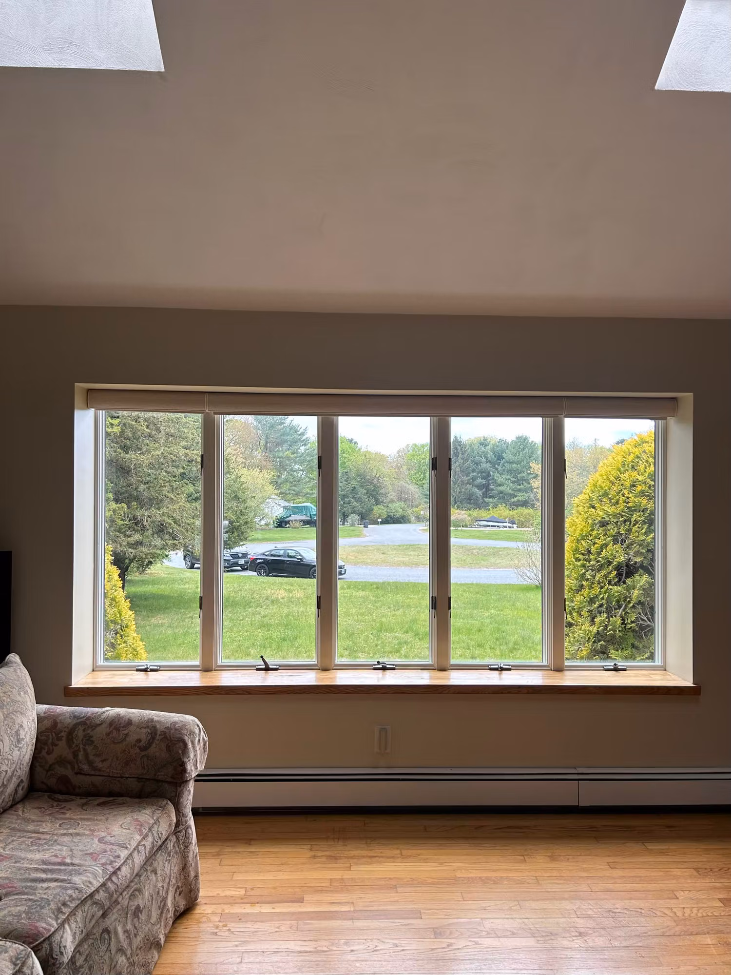A wide five-pane picture window in a living room overlooking a green lawn, with a sofa nearby.