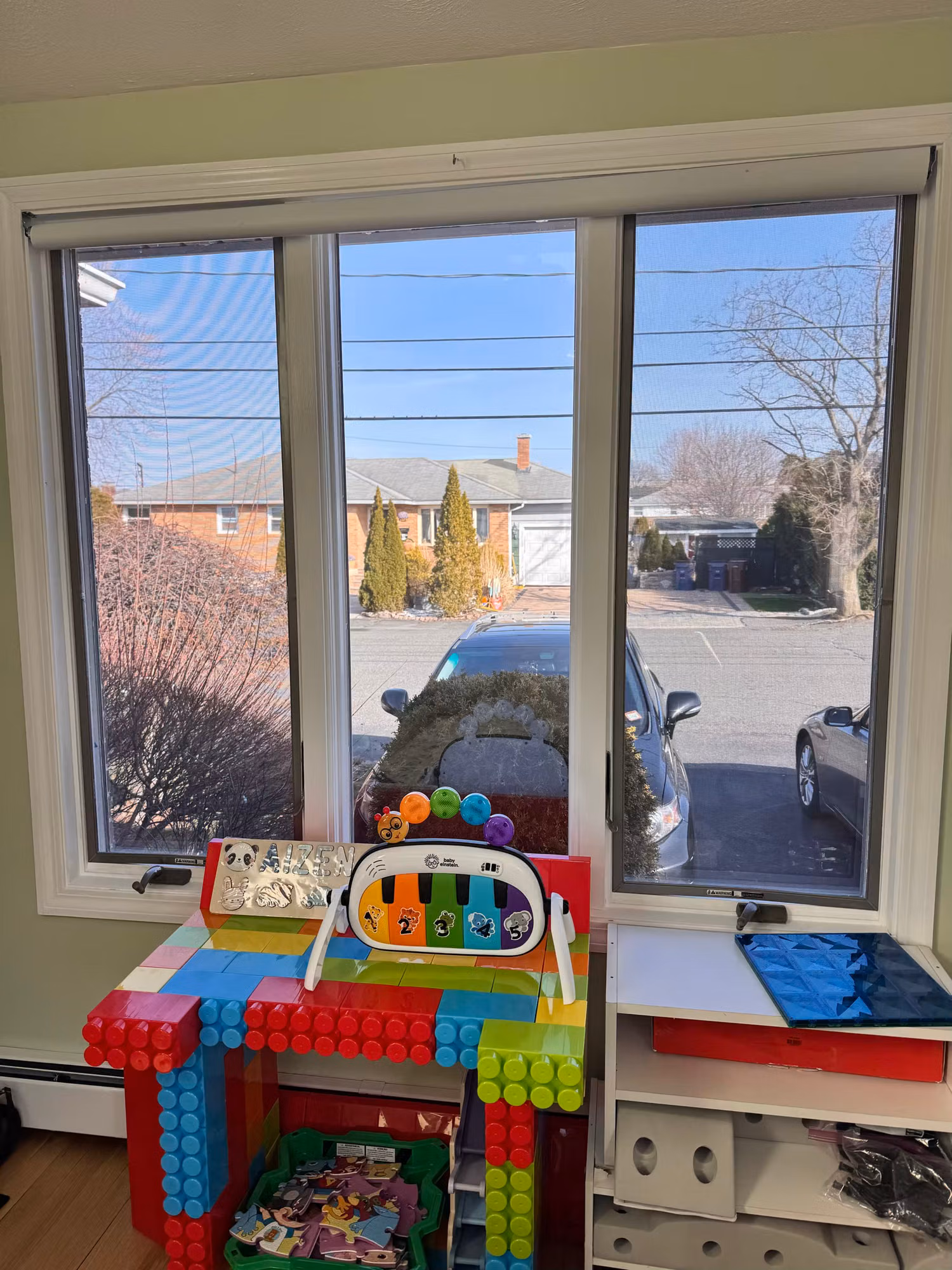 Sliding window in a child's playroom with toys and building blocks below, overlooking a street view.