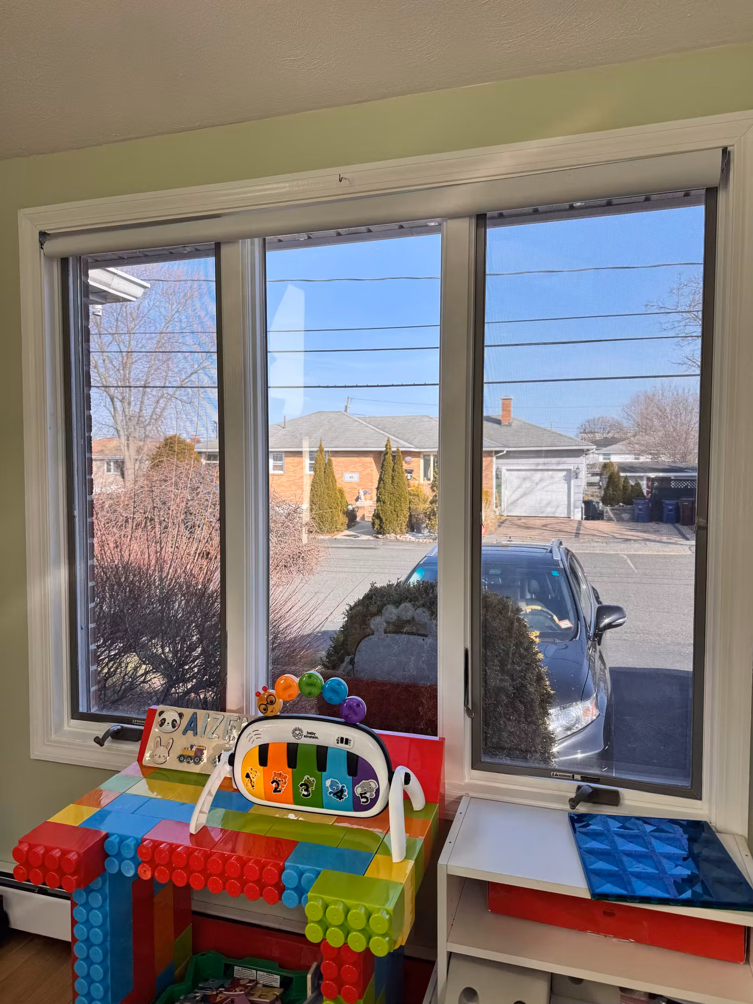 Wide slider window in a children's playroom with colorful toys, looking out toward neighboring homes.