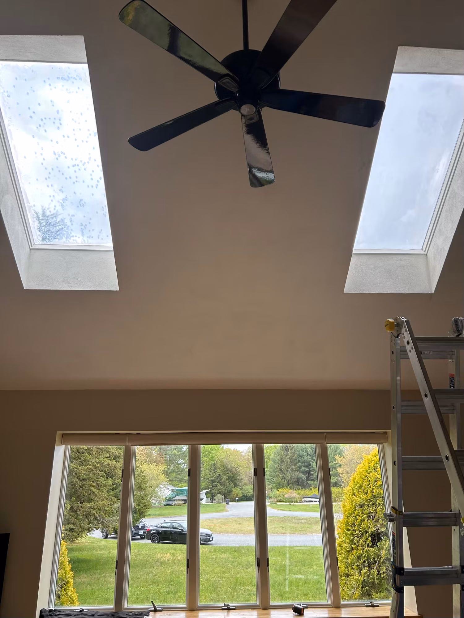 Two angled skylights in a vaulted ceiling above a picture window, with a ladder set up for film installation.