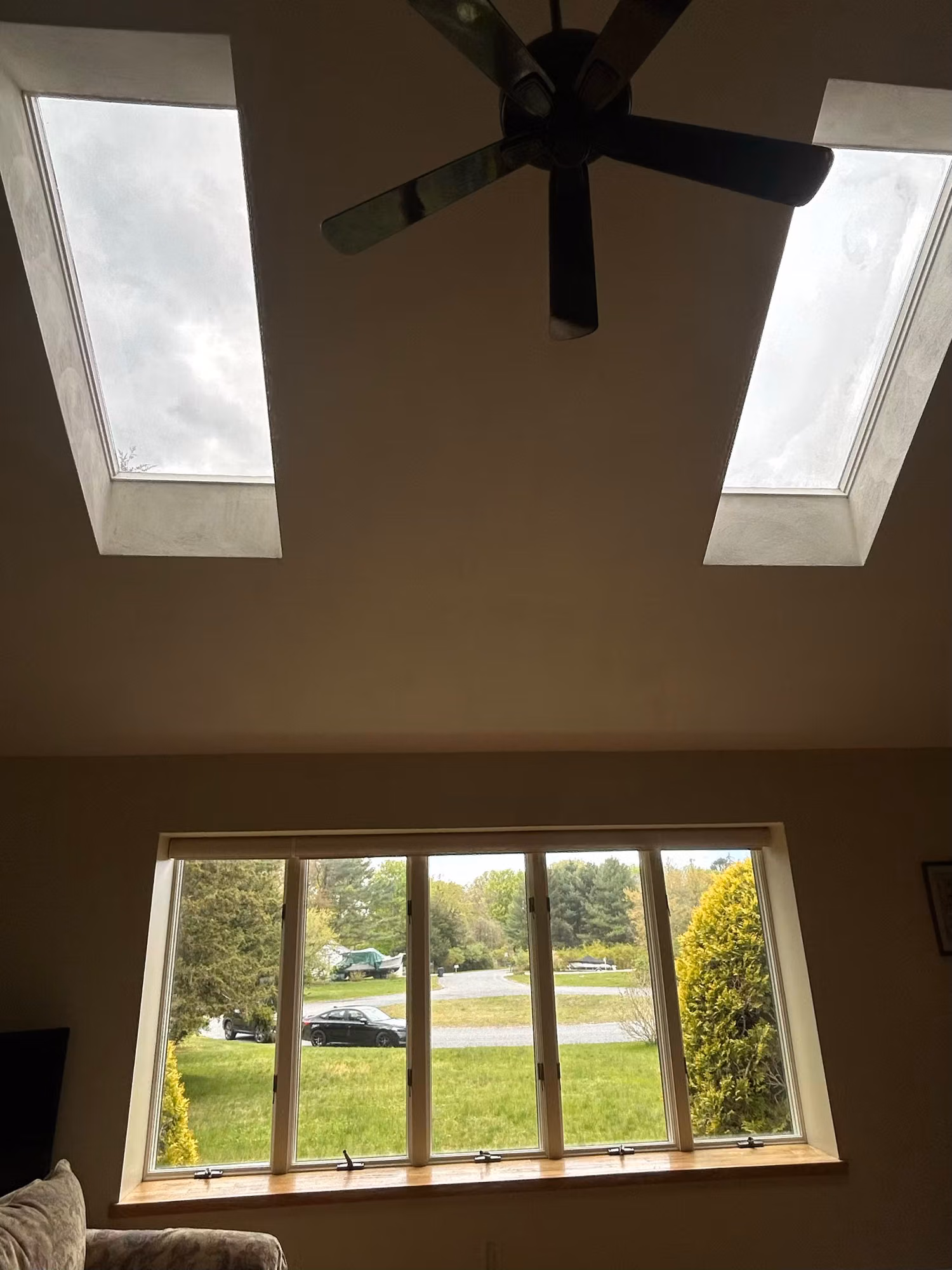 Two angled skylights in a vaulted ceiling above a casement window framing a view of trees and lawn.