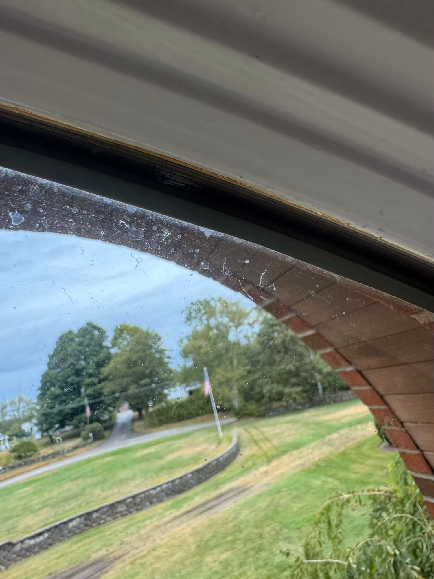 Close-up of an arched window frame corner looking out toward a driveway, stone wall and lawn during a film install.