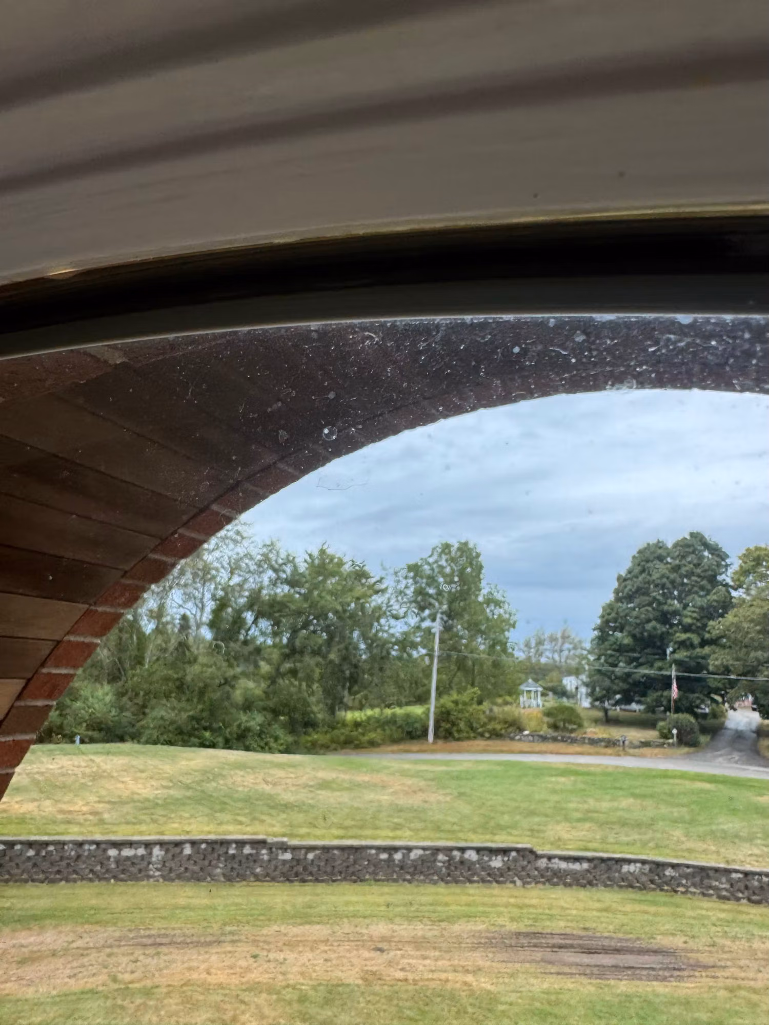 Close-up of an arched window frame edge with wood and brick trim looking out over a lawn during installation.