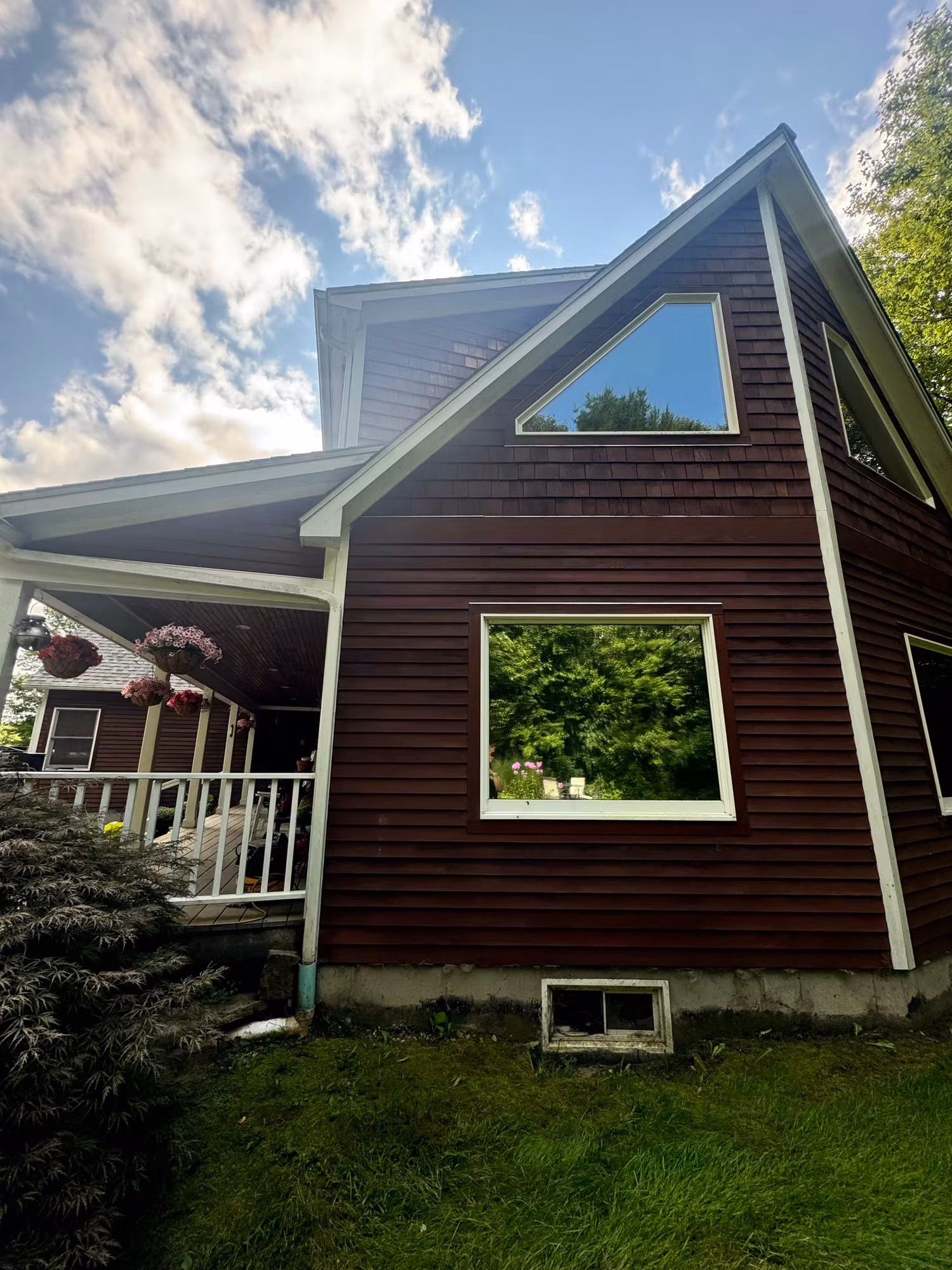 Side of a dark brown home with a triangular gable window and a large picture window above the foundation.