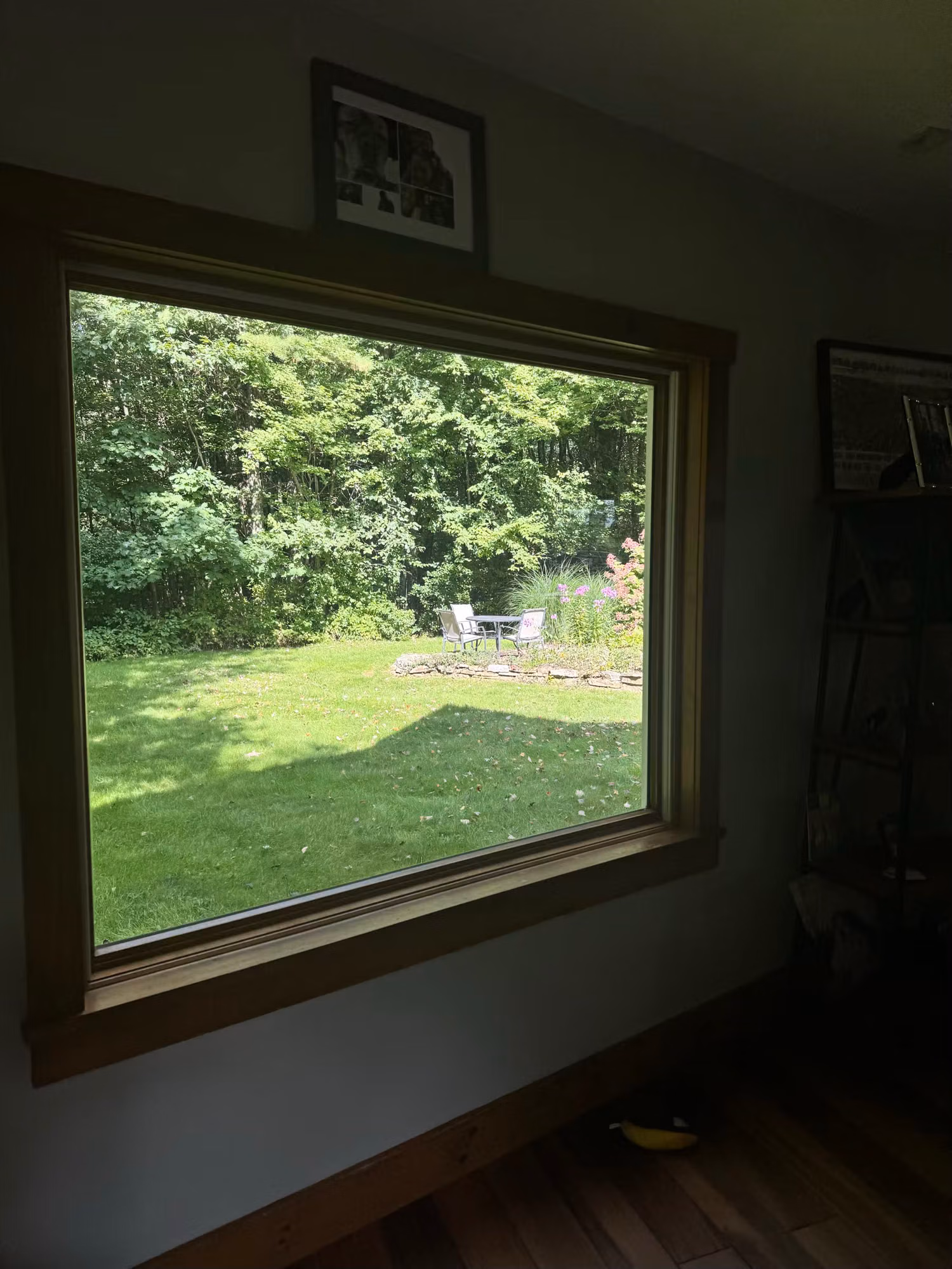 Large wood-framed picture window in a living room looking out to a green backyard and patio.