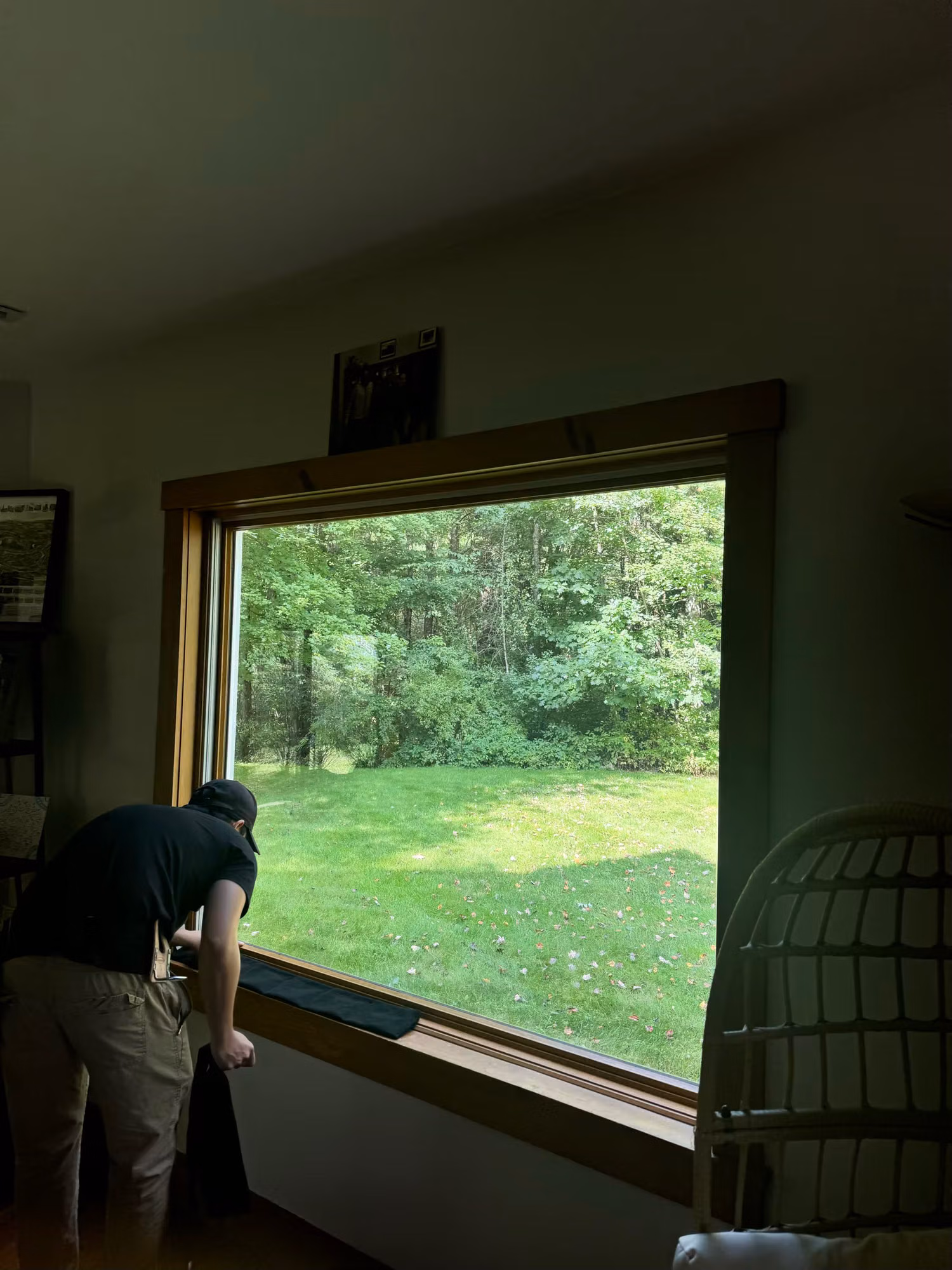 Installer working at the sill of a large wood-framed picture window during a window film installation.