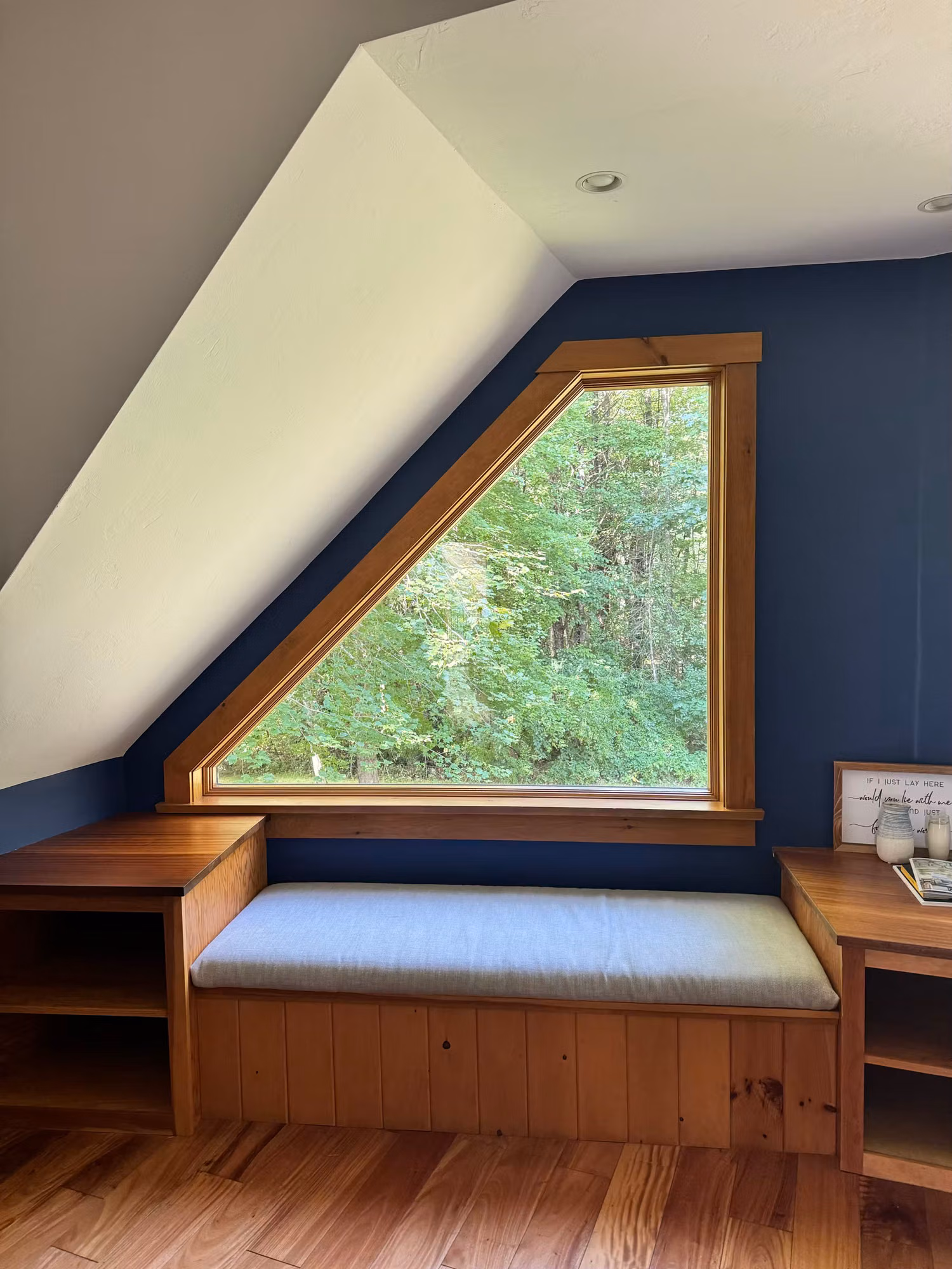 Triangular wood-framed loft window above a built-in window seat with navy accent walls in a bedroom nook.