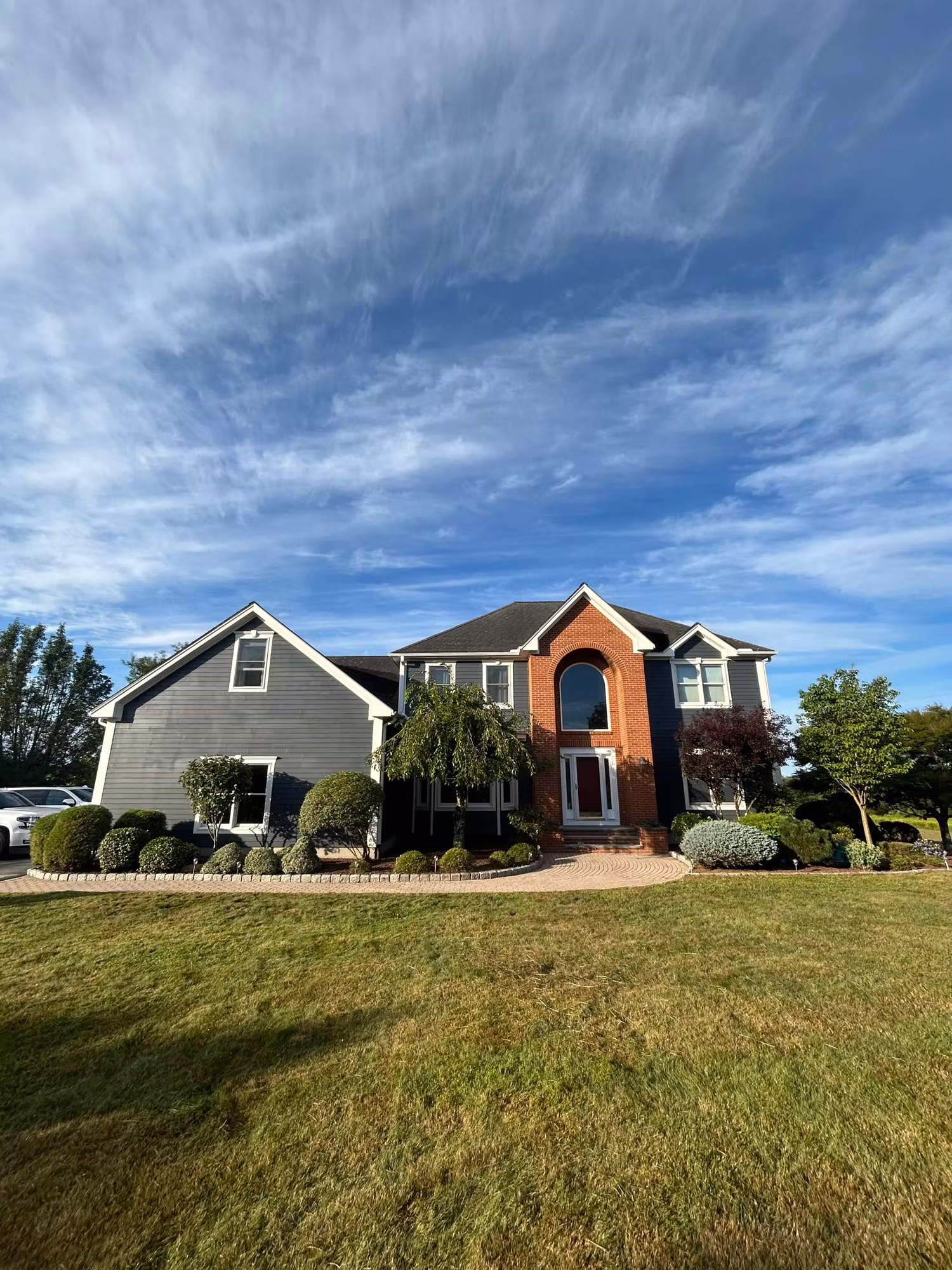 Two-story home with gray and brick siding and an arched entry window under a clear blue sky.