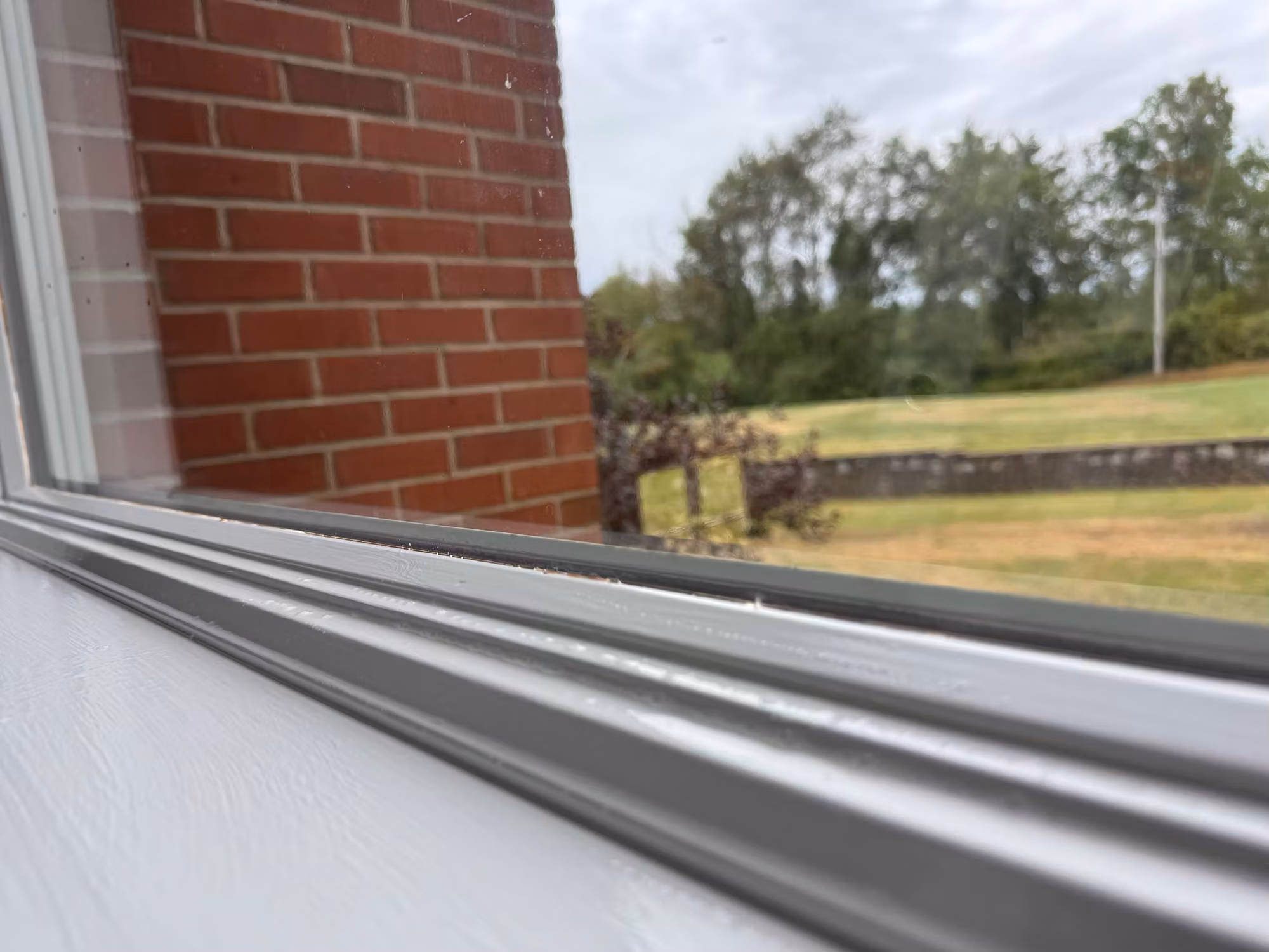 Close-up of a residential window frame edge looking out to a brick wall and green lawn during a film installation.