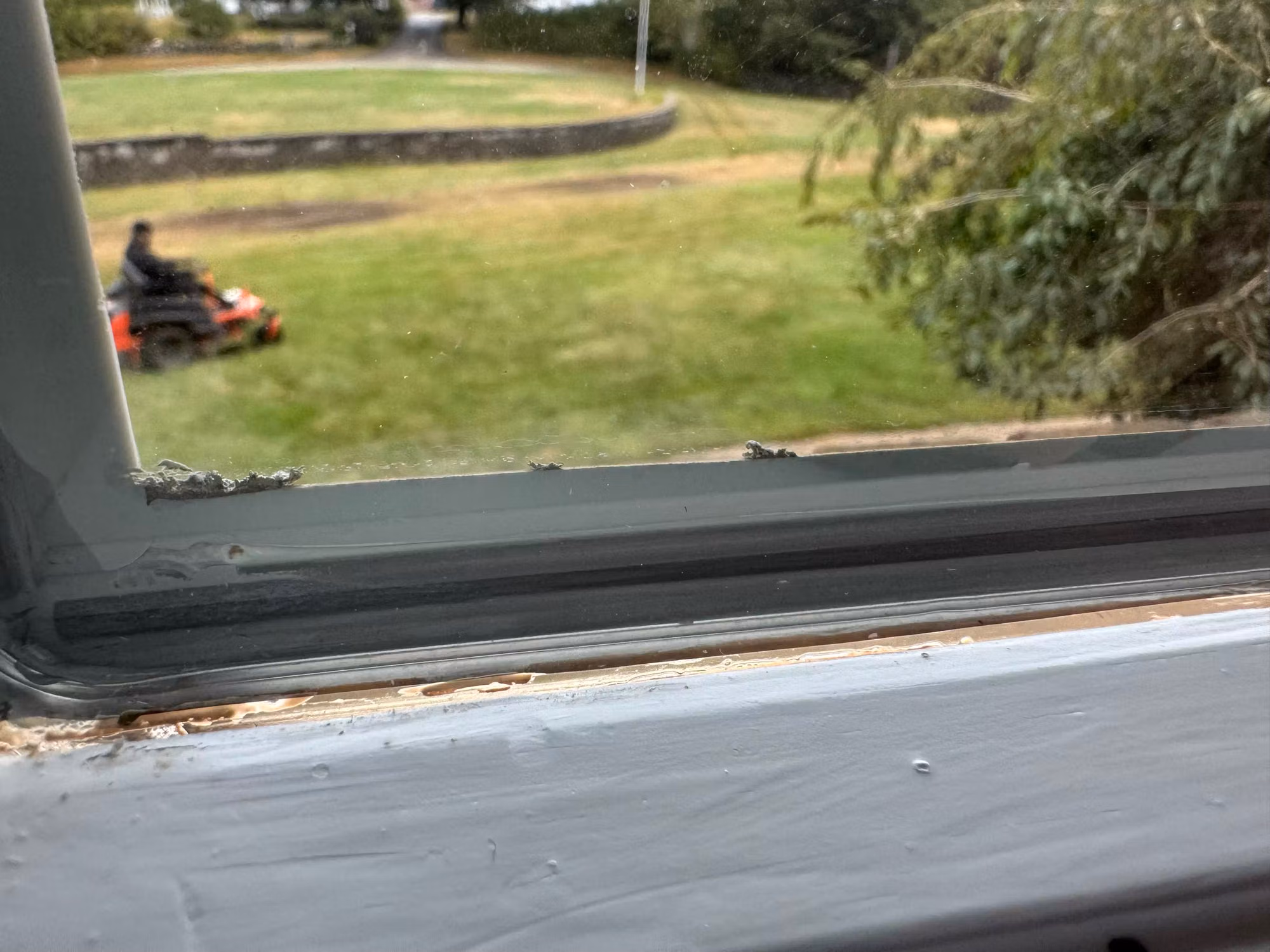 Close-up of a window sill and frame edge looking out to a lawn with a riding mower during a residential film job.