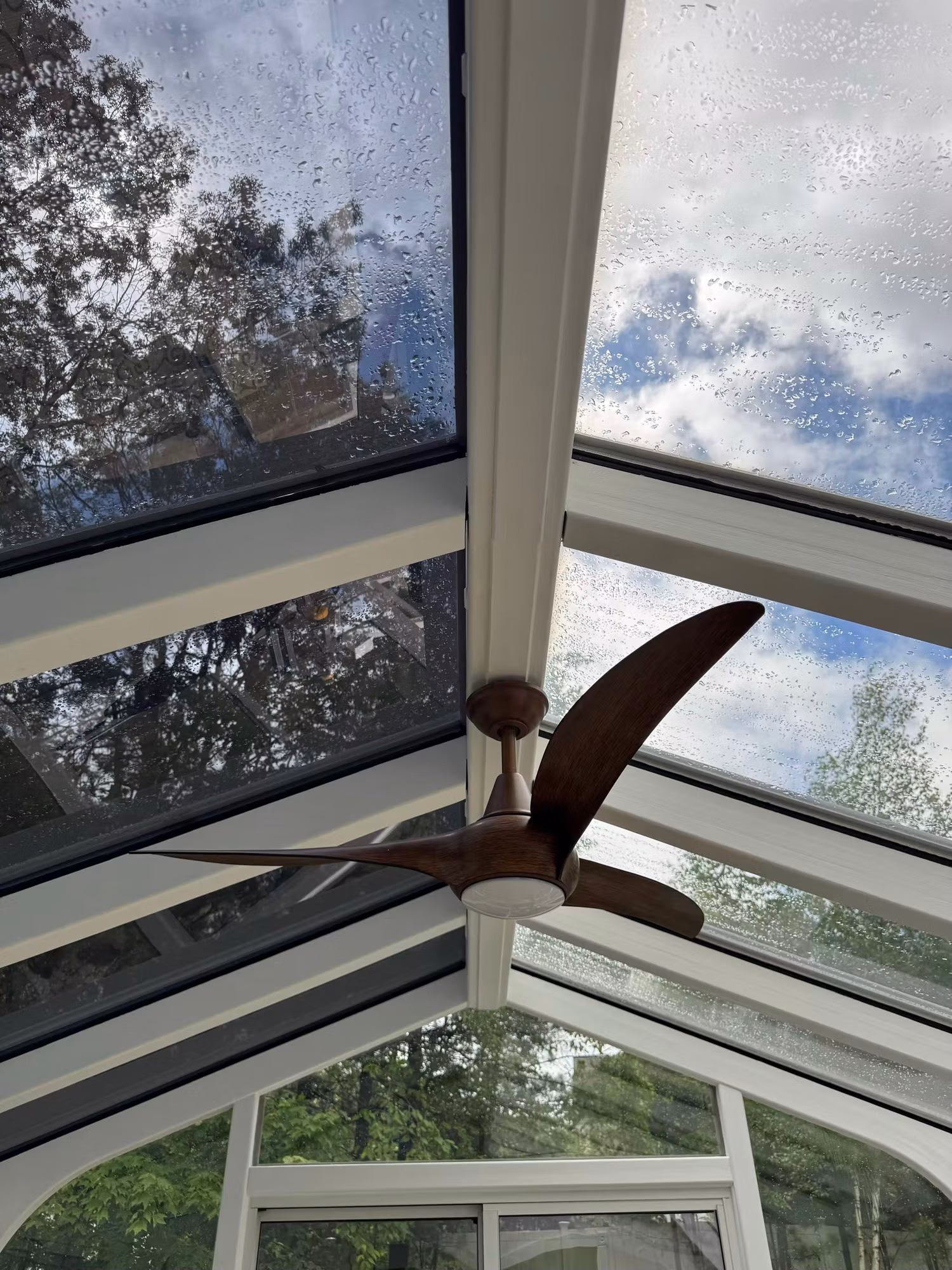 Sloped sunroom glass roof panels with solar control film reducing heat and glare beneath a ceiling fan.