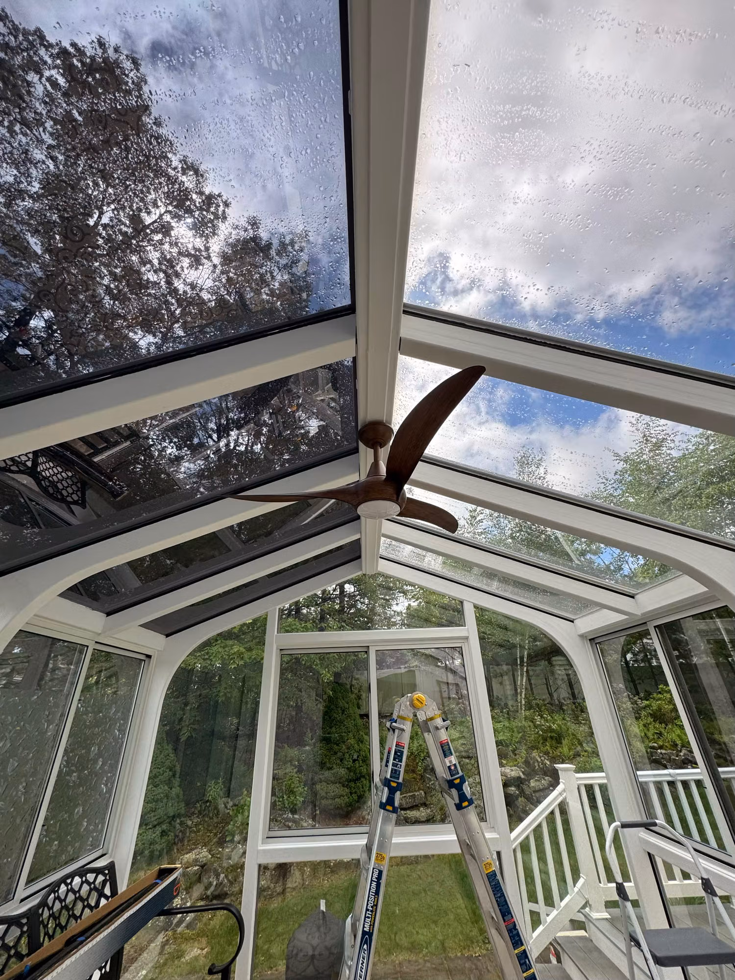 Solar control film being installed on a gabled sunroom glass roof with ladders set up on the floor below.