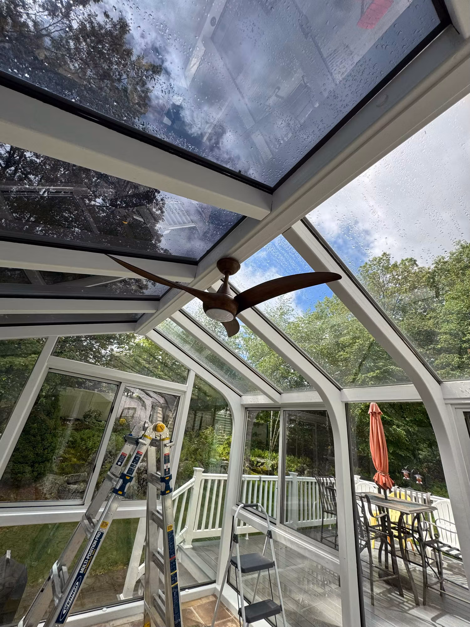 Sunroom glass roof getting solar control film with ladders and equipment in place overlooking the rear deck.